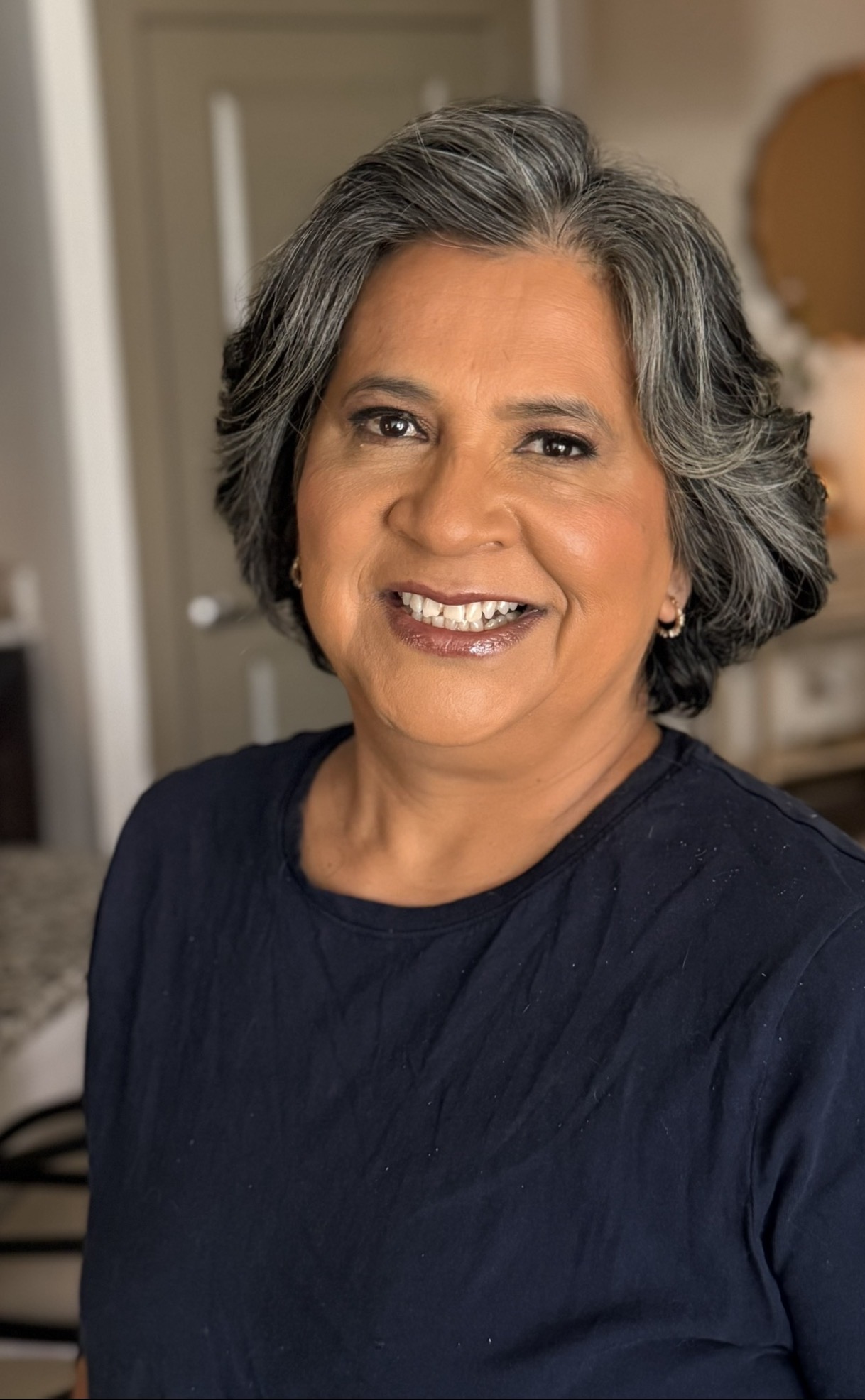 Smiling woman with short gray hair wearing a dark shirt indoors.