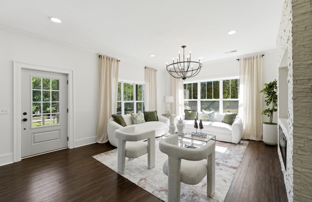 Bright living room with white walls, large windows, white furniture, chandelier, and hardwood floor.