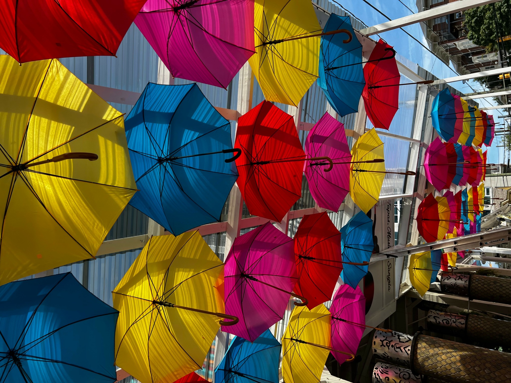 Colorful umbrellas hanging above a street, with buildings and people in the background.