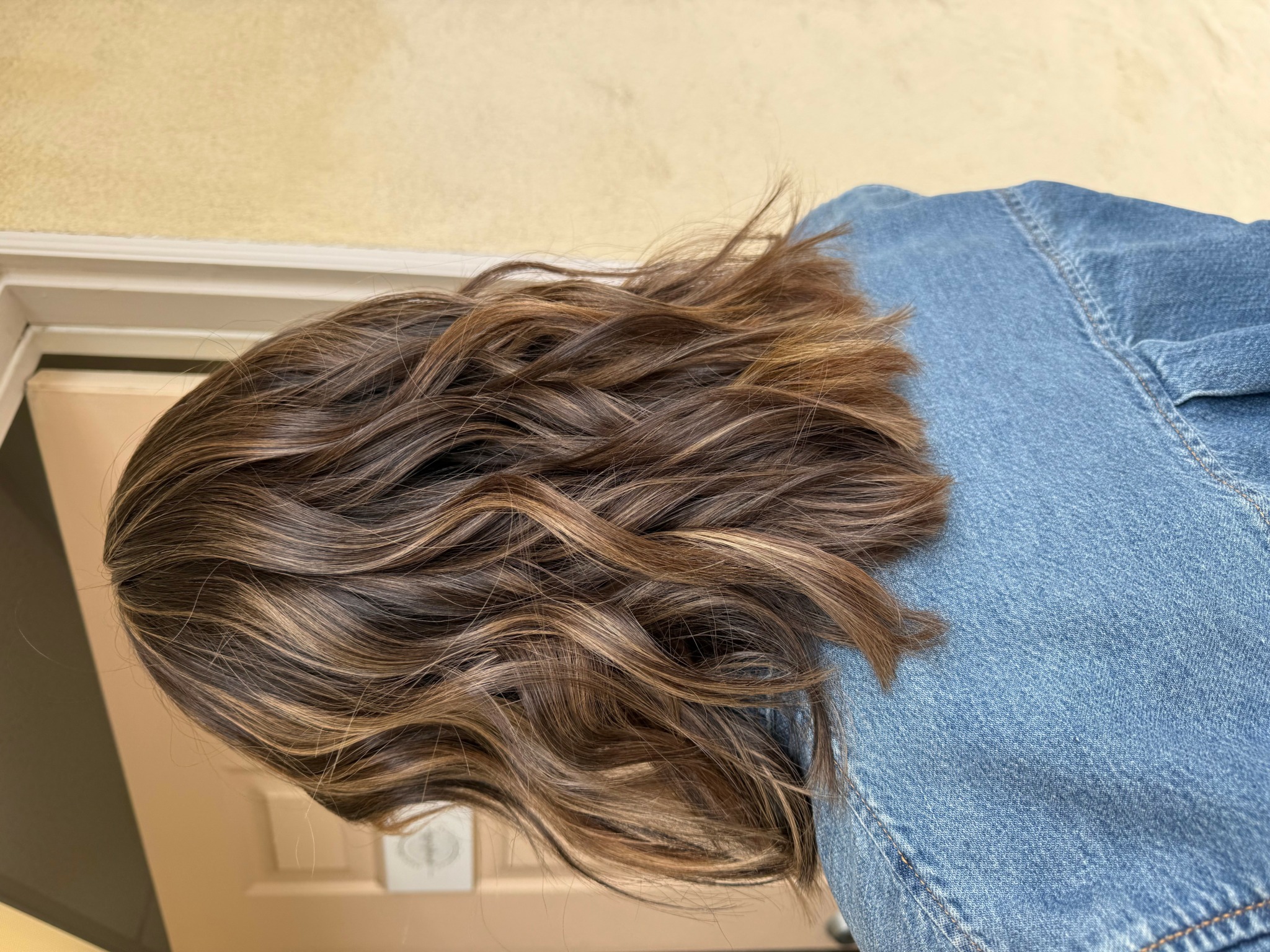 Person with wavy, shoulder-length hair wearing a denim jacket, facing sideways.