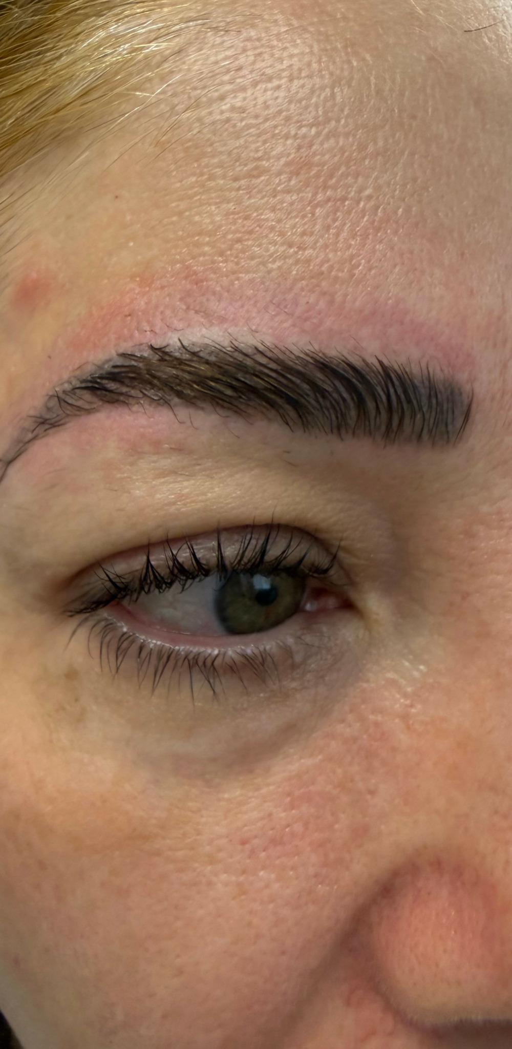 Close-up of a person's eye, eyebrow, and forehead with visible skin texture and makeup.