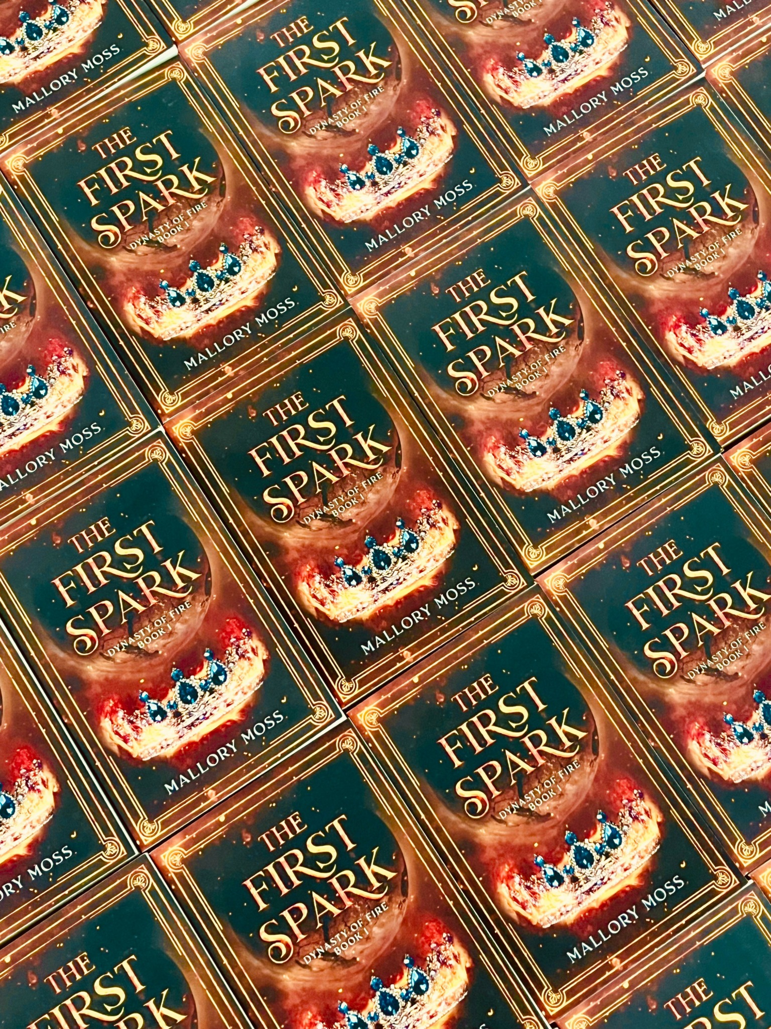 Multiple copies of a book titled 'The First Spark' by Mallory Moss arranged in a pattern.