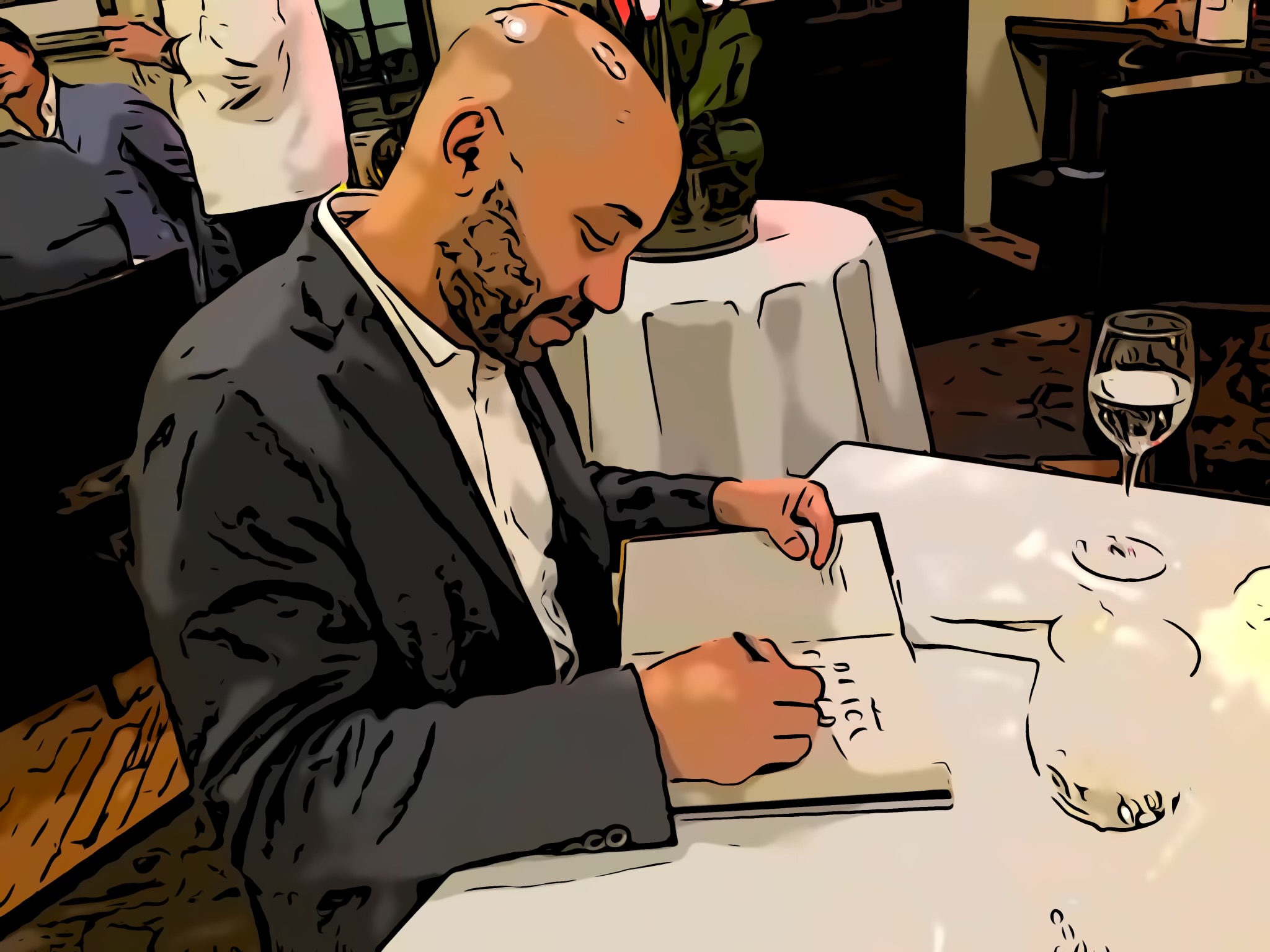 Man in suit signing a book at a table with a glass of wine and a water pitcher.