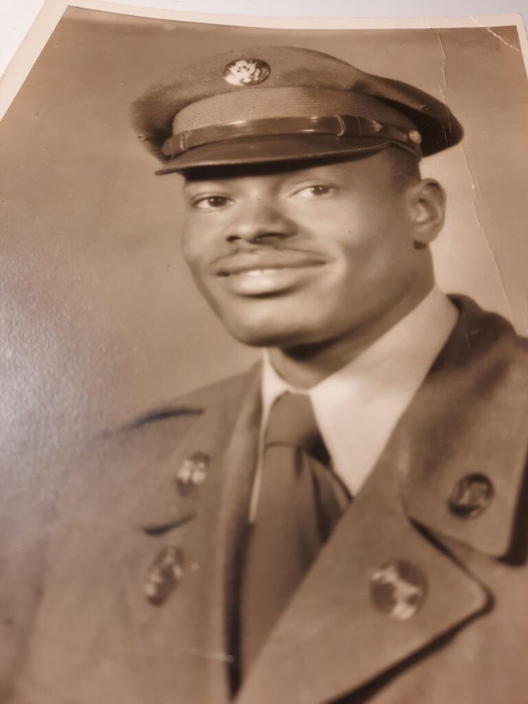 Black and white portrait of a man in a military uniform and cap, smiling, with a plain background.