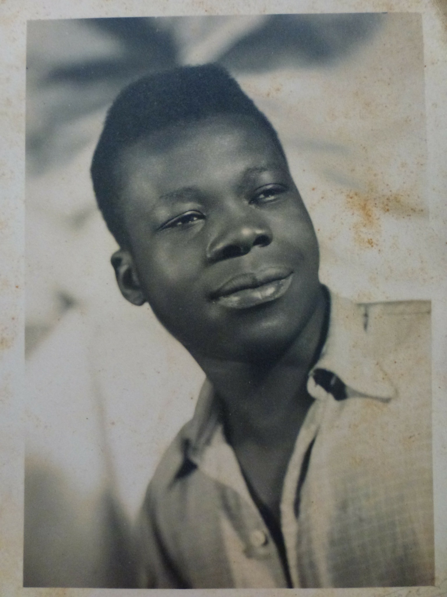 Young boy with short hair wearing a collared shirt, looking slightly to the side outdoors.