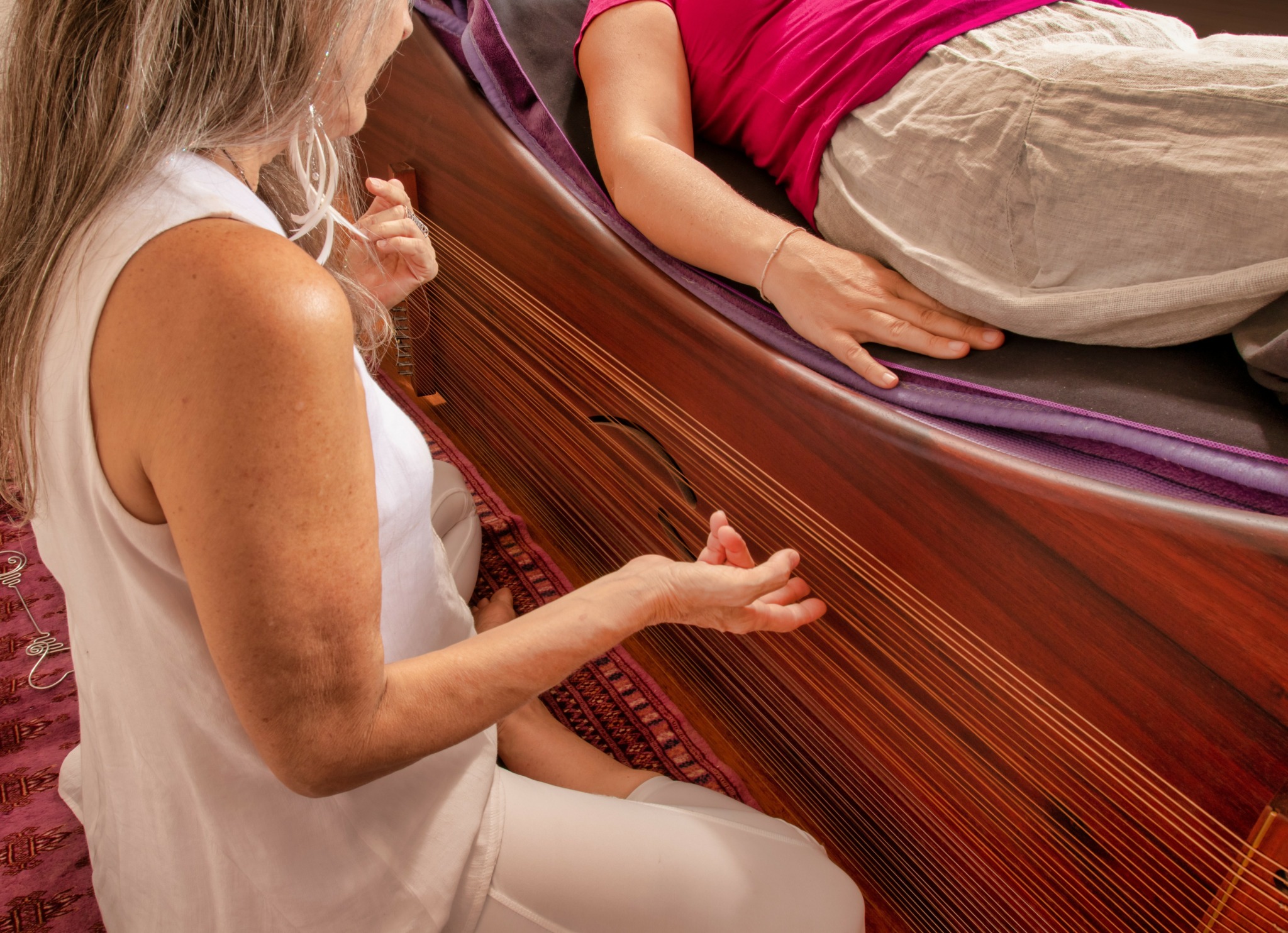Person sitting on the floor with hand extended, another person lying on a curved wooden surface, both in casual clothing.