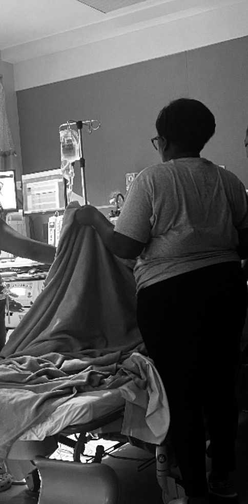 Person standing beside hospital bed with medical equipment and a patient lying down.