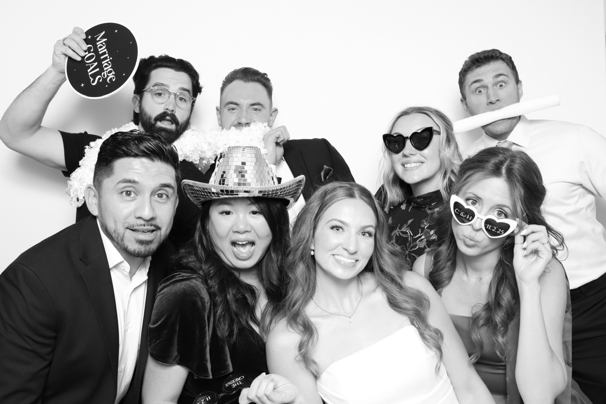 Group of seven people smiling, some wearing sunglasses and party accessories, celebrating together.