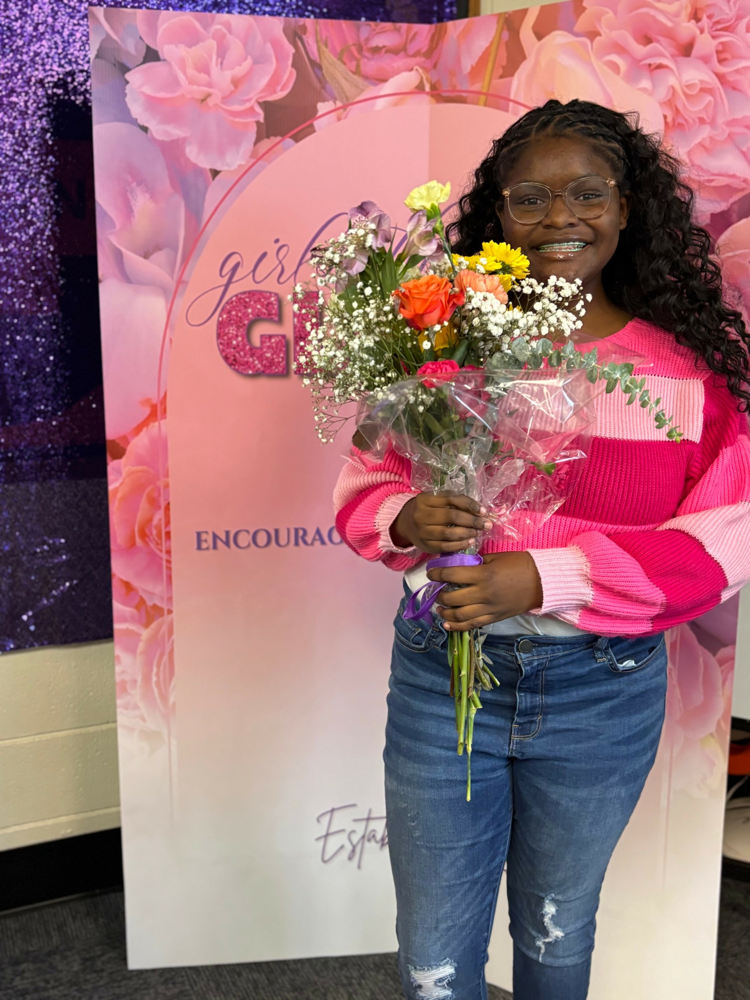 Smiling woman holding a bouquet of flowers in front of a pink floral backdrop with text.