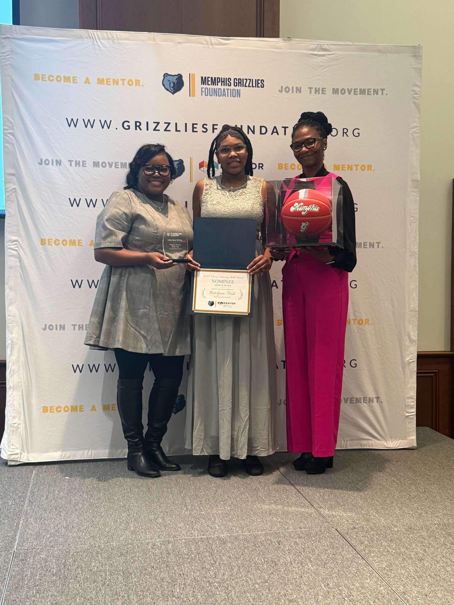 Two women standing in front of a white backdrop, one holding a certificate, the other with a backpack, both smiling.