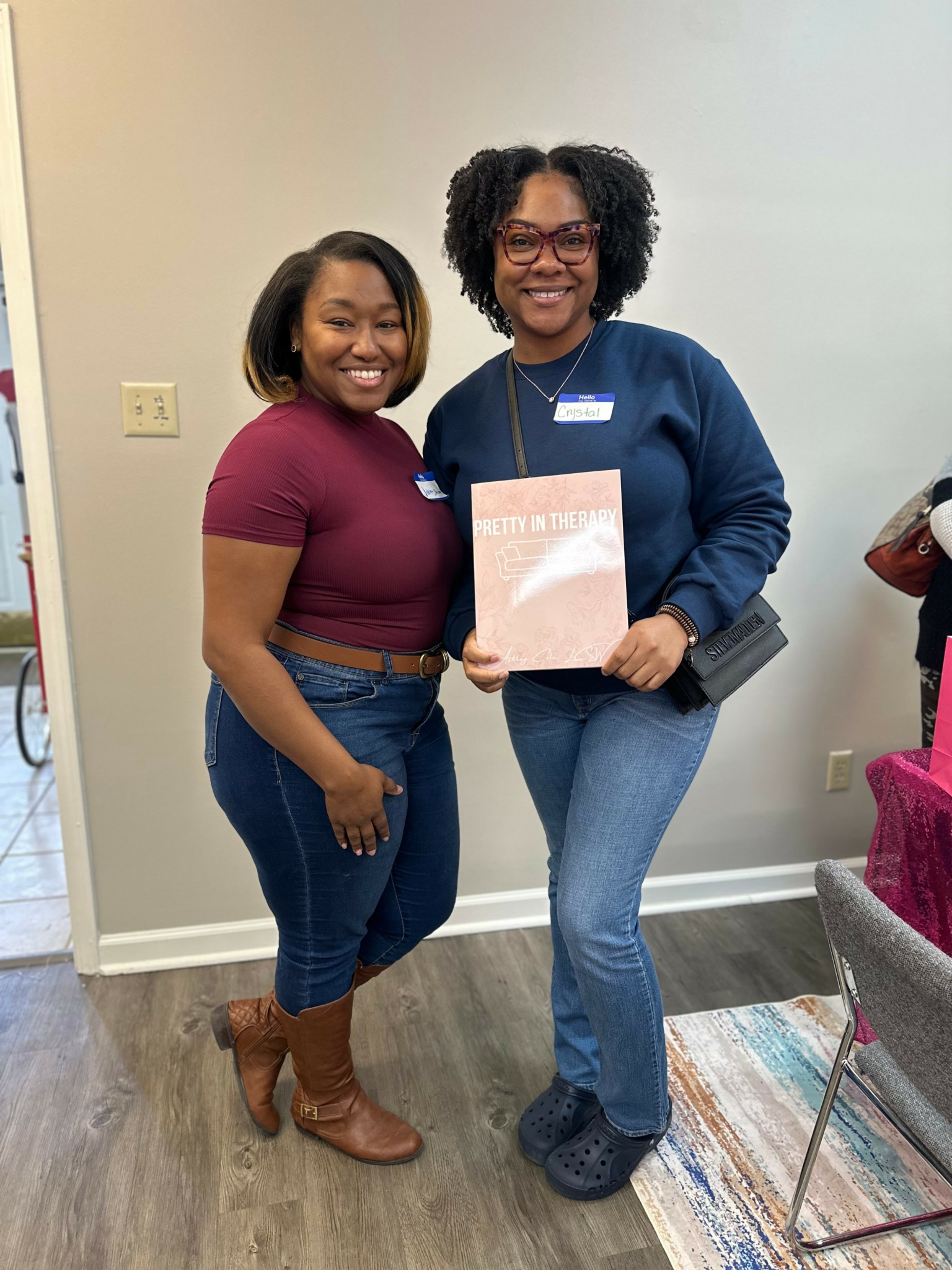 Two women smiling indoors, one holding a certificate or document, standing close together.