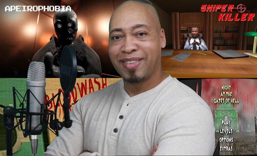 A man smiling in front of a gaming setup with a microphone, gaming screens, and posters, including one with a masked figure.