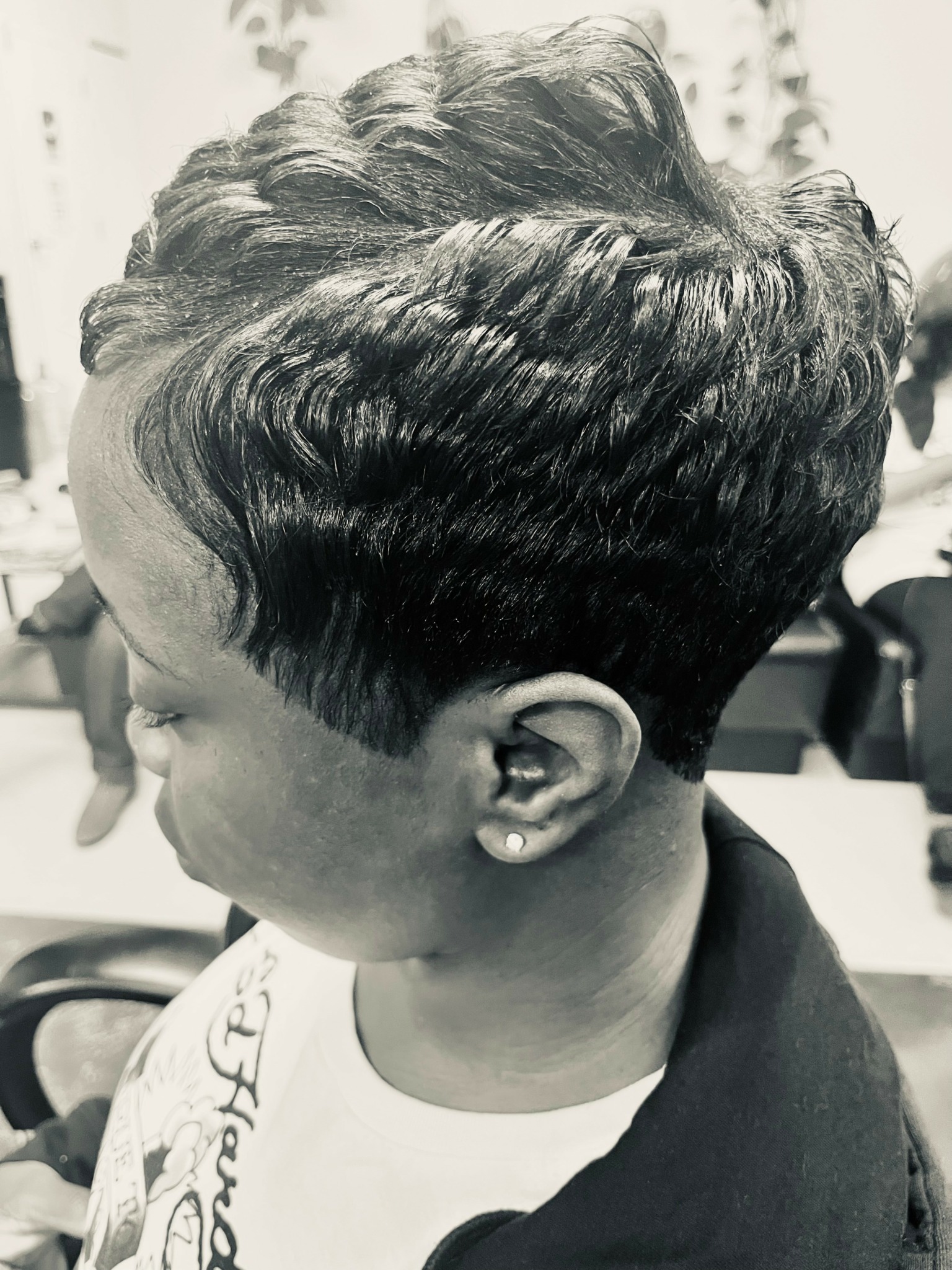 Side view of a person with short, styled hair and an earring, in a salon setting.