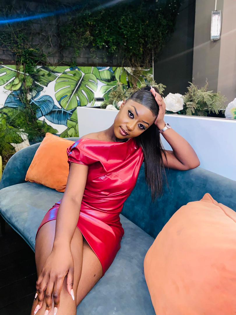 Woman in red satin dress sitting on a sofa with orange pillows, outdoors with greenery background.