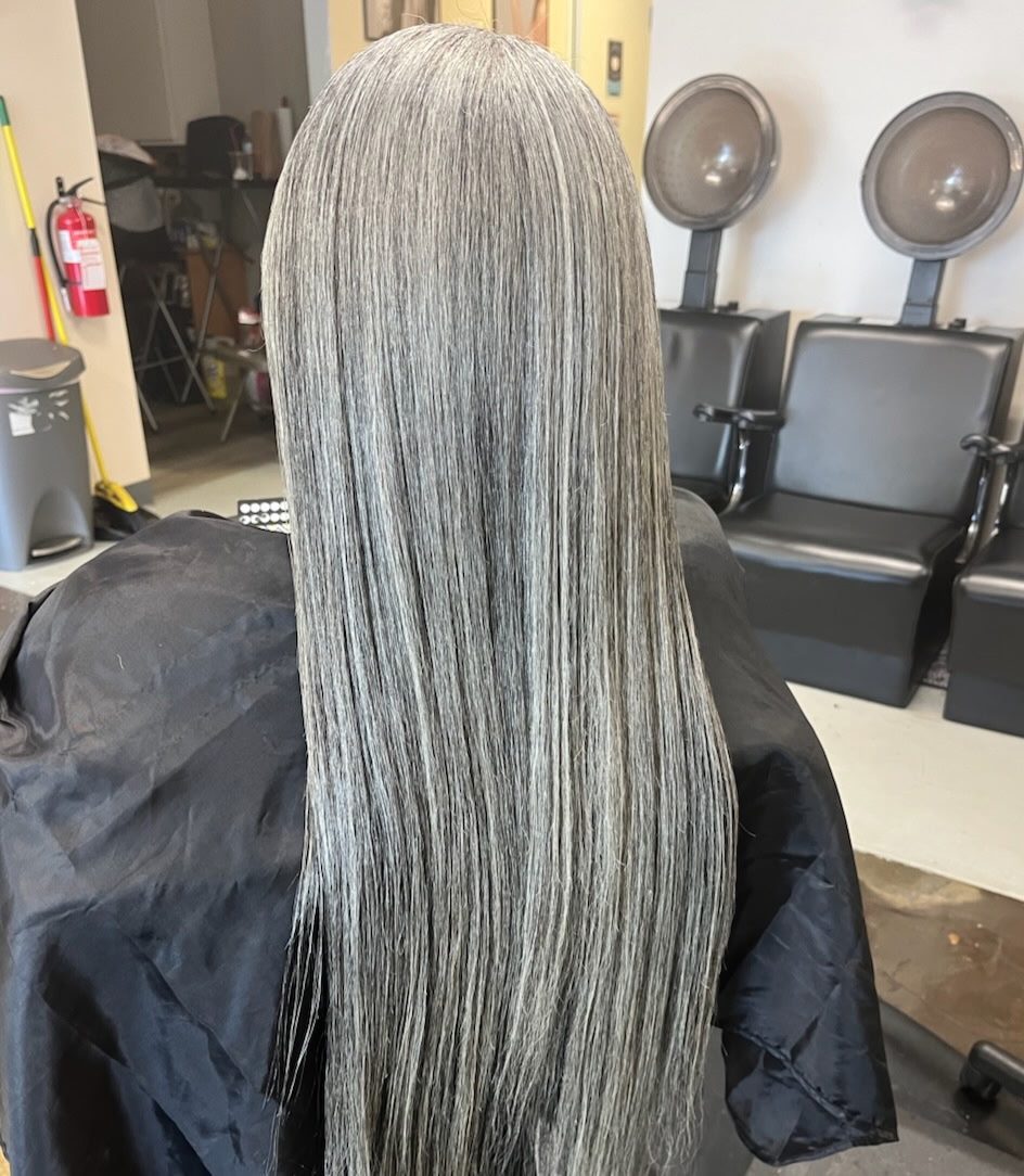 Back view of a person with long, straight, silver-gray hair in a salon.