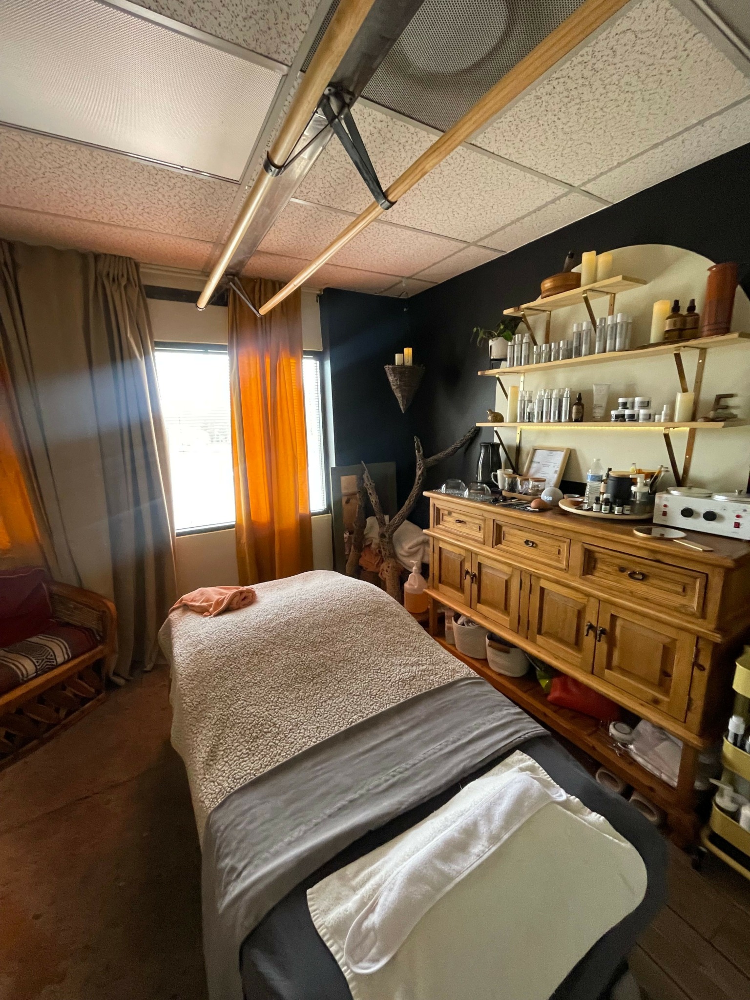 Room with bed, wooden furniture, shelves, and a window with curtains, viewed from the doorway.