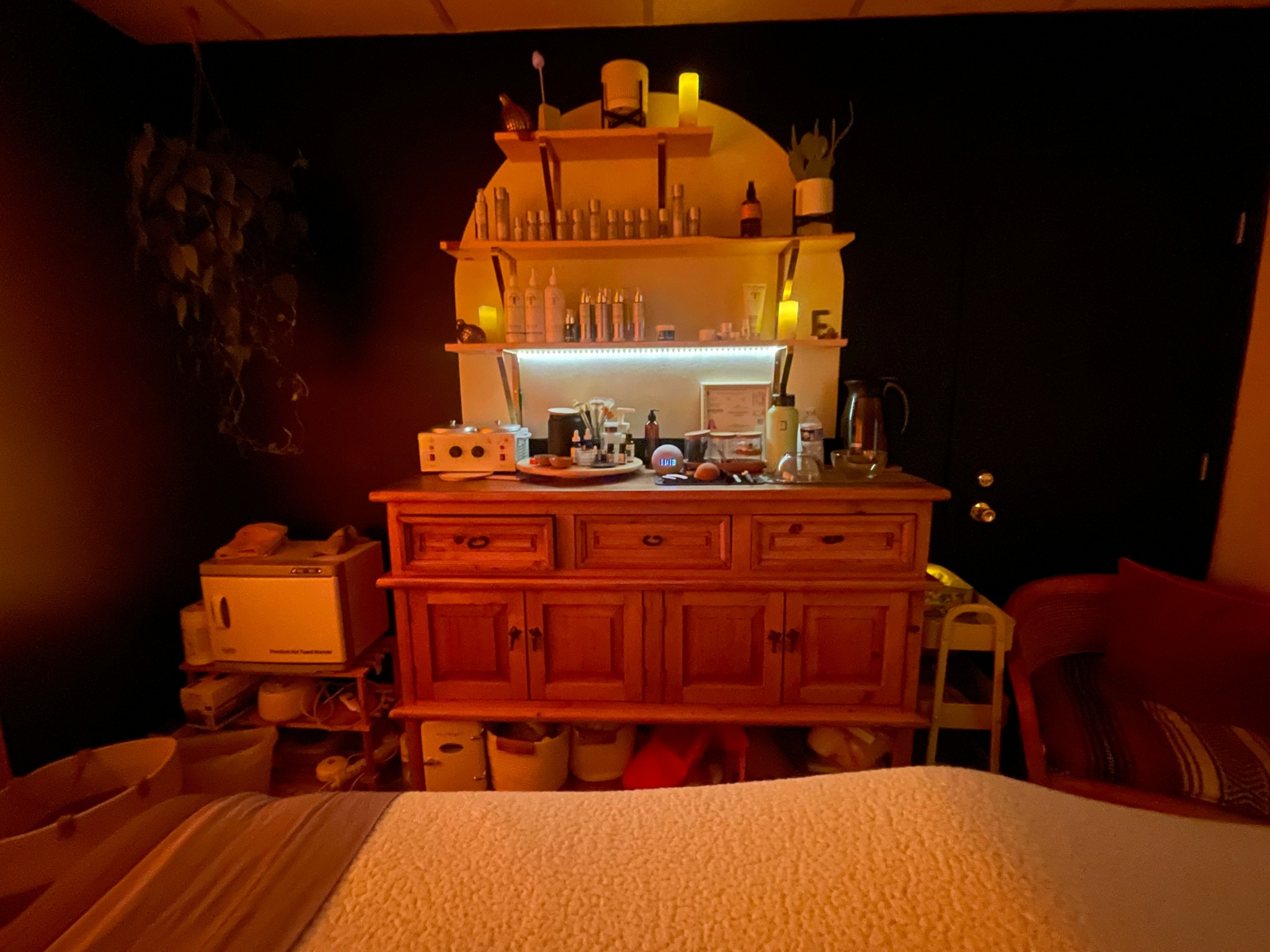 Wooden cabinet with shelves above, illuminated by warm lighting, surrounded by various objects in a cozy room.