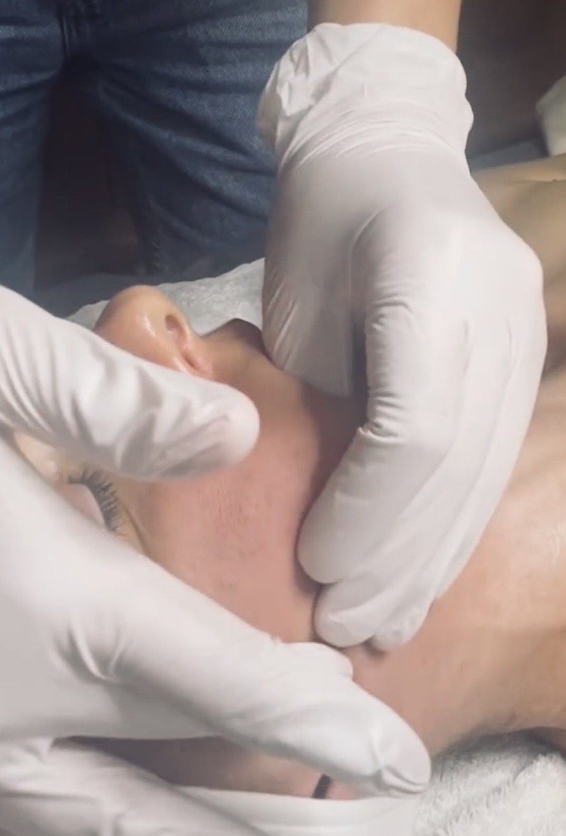 Person lying down with a gloved hand touching their face, in a medical setting.