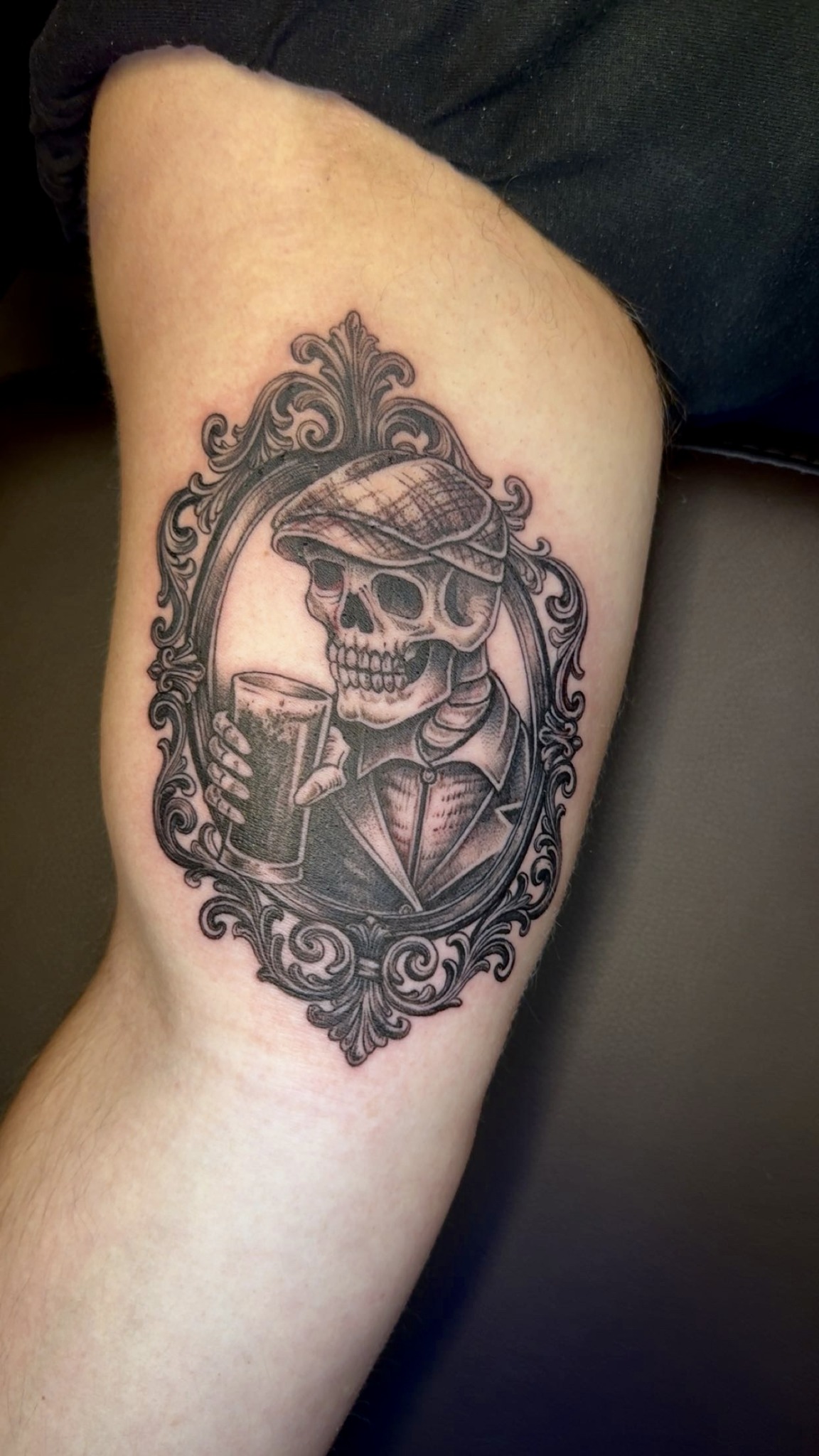 Skull wearing a cap inside an ornate oval frame with decorative details.