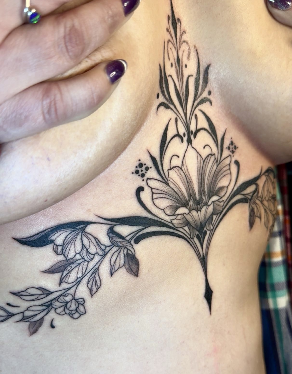 Black floral tattoo on person's chest with detailed petals and leaves, extending upward and downward.