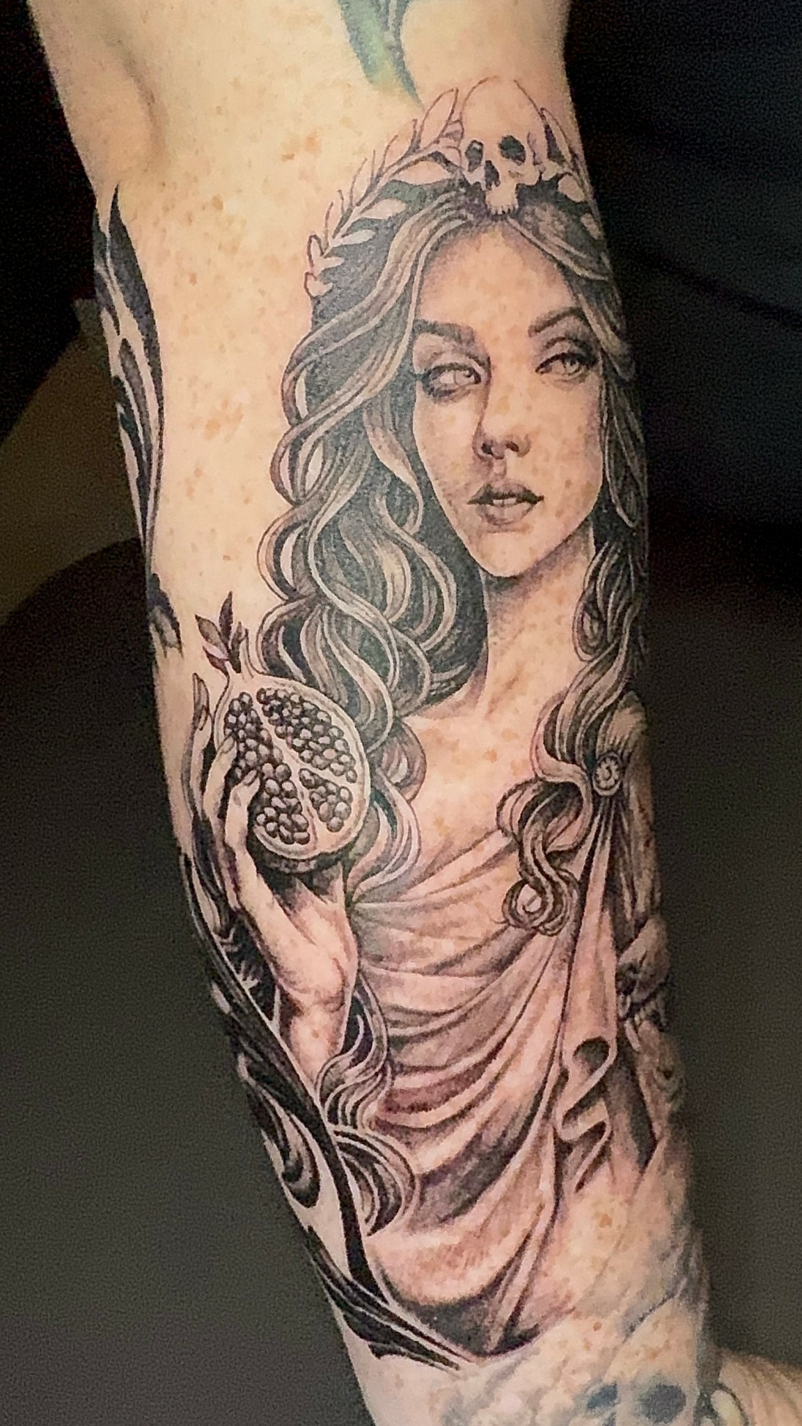 Tattoo of a woman with flowing hair holding a seashell, wearing a crown, in black and gray ink.
