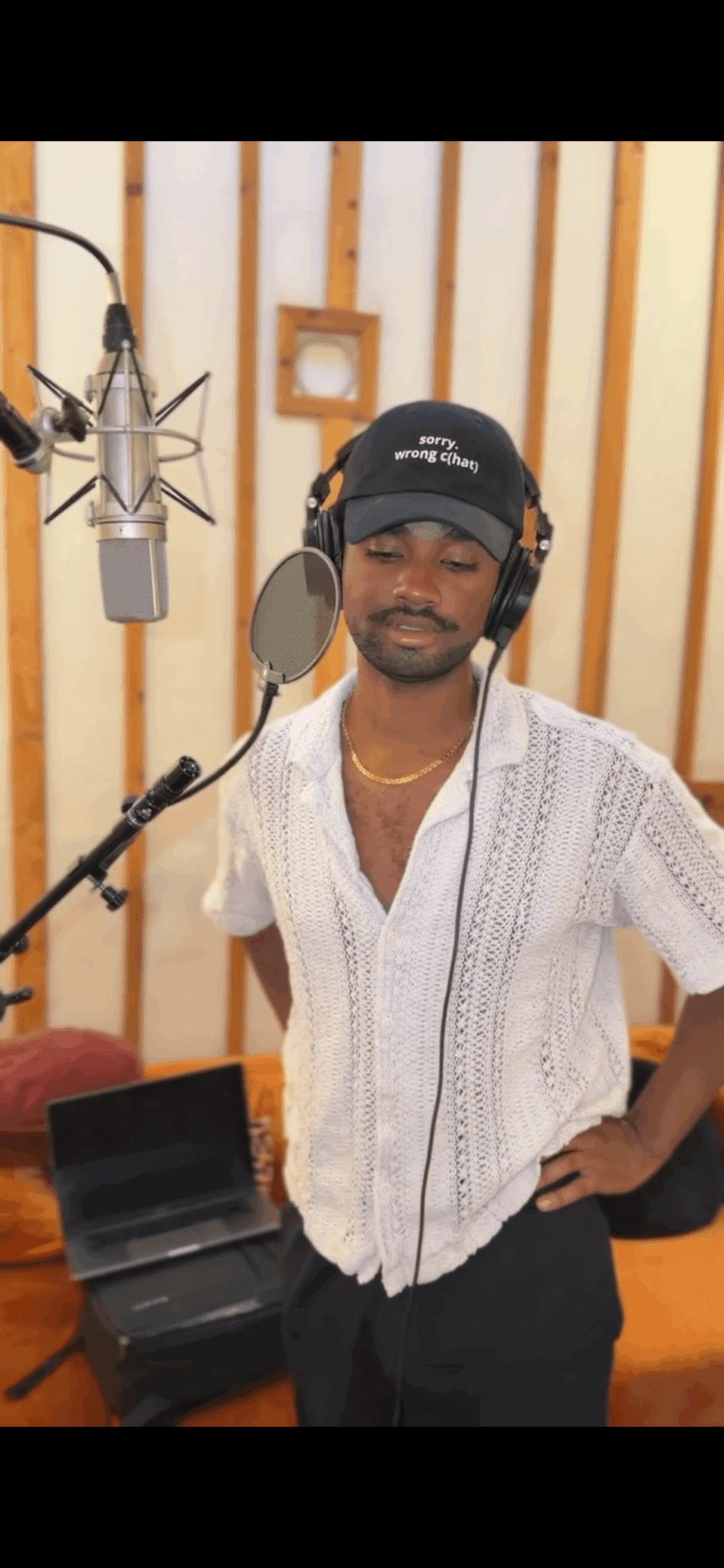 Man wearing headphones and a white shirt standing in a recording studio with microphone and soundproof walls.