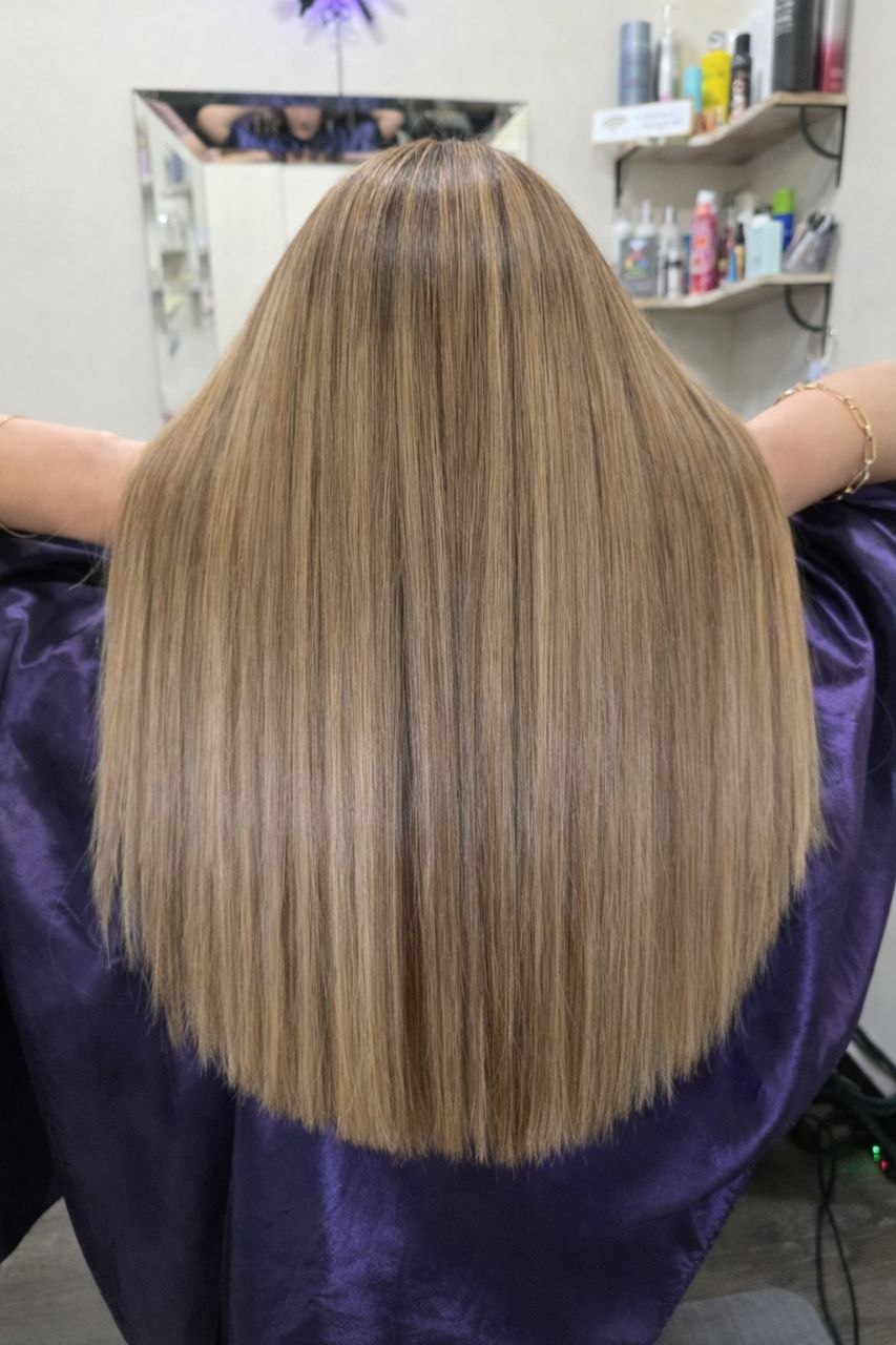 Back view of a person with long, straight, blonde hair in a salon setting.