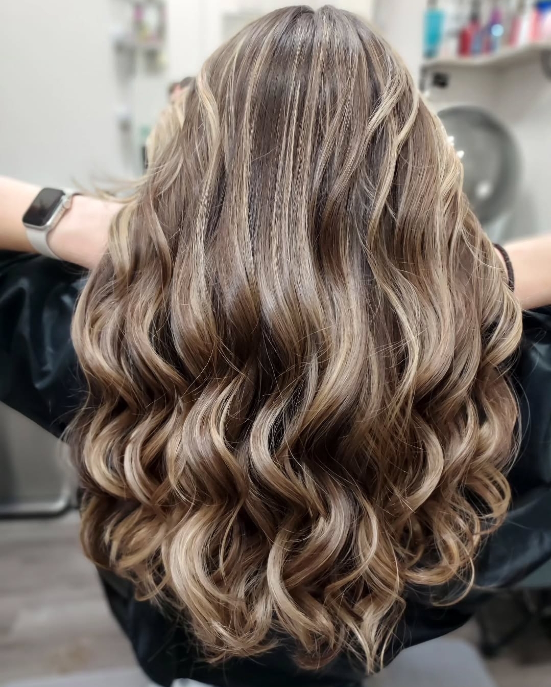 Back view of long, wavy, blonde hair with highlights, styled in loose curls.