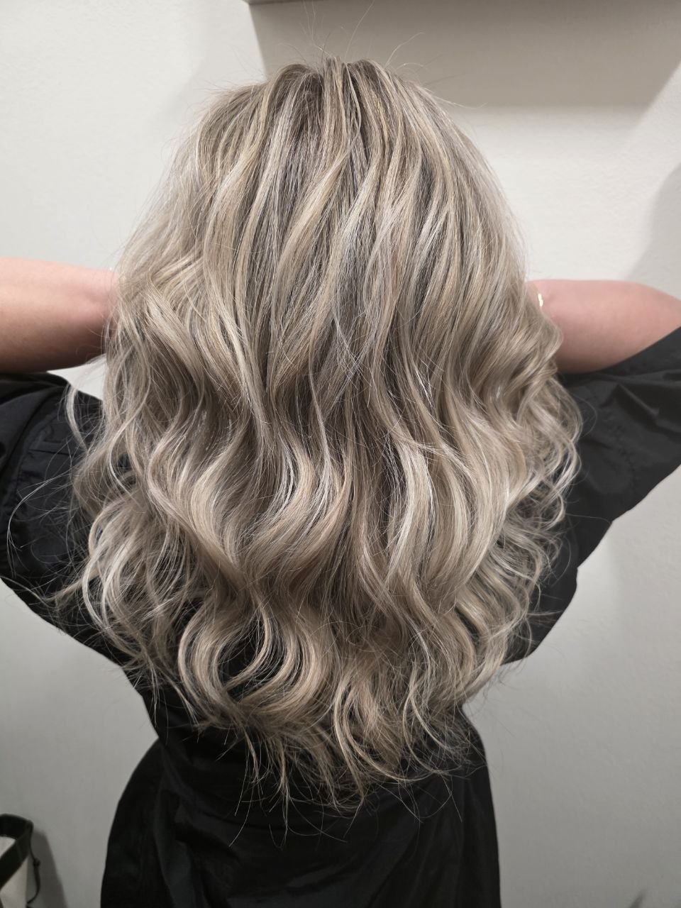 Back view of wavy, blonde hair with darker roots, styled in loose curls.