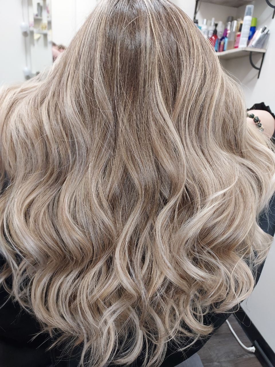 Long, wavy, blonde hair with highlights, viewed from the back in a salon setting.