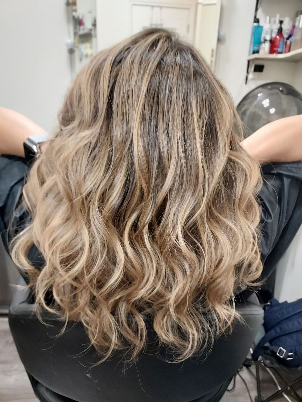 Back view of a person with long, wavy, blonde hair sitting in a salon chair.