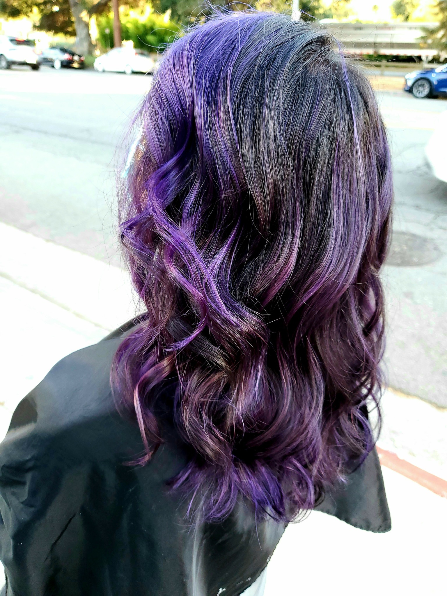Person with wavy hair dyed purple and black, standing outdoors on a sunny day.
