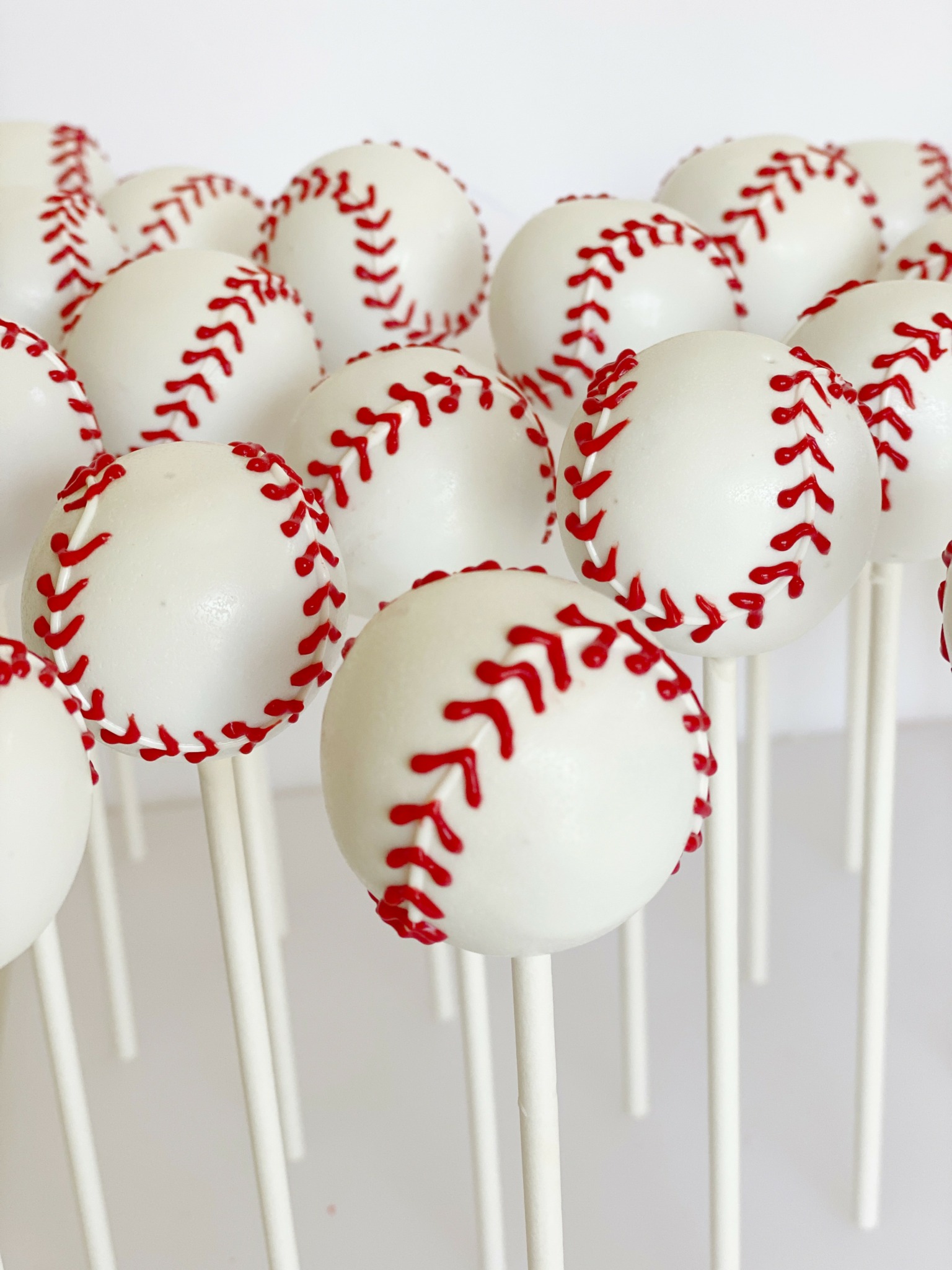 White spherical objects with red stitching pattern on sticks, resembling baseballs, arranged closely together.