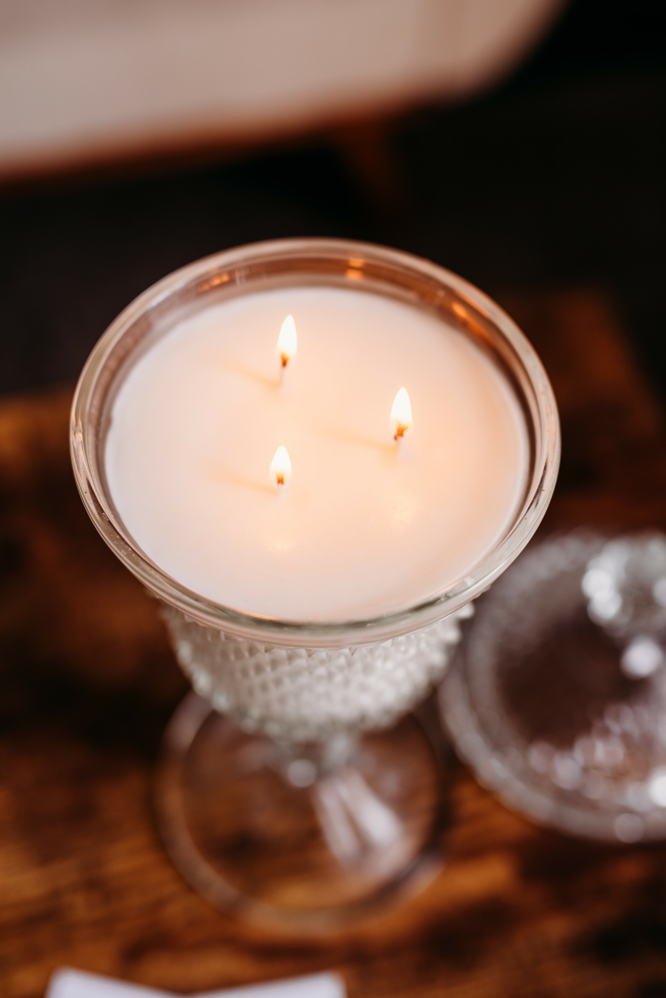 Glass candle holder with three lit candles, on a wooden surface, with a blurred background.