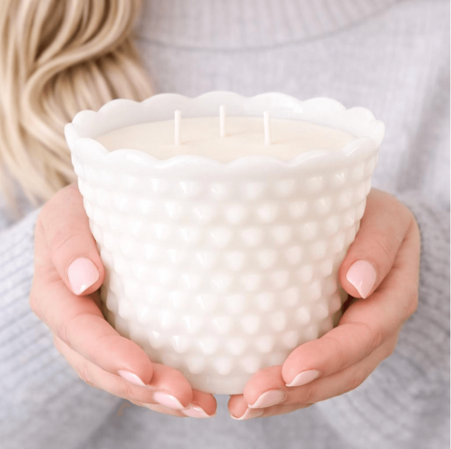 Person holding a white textured candle holder with three wicks inside.