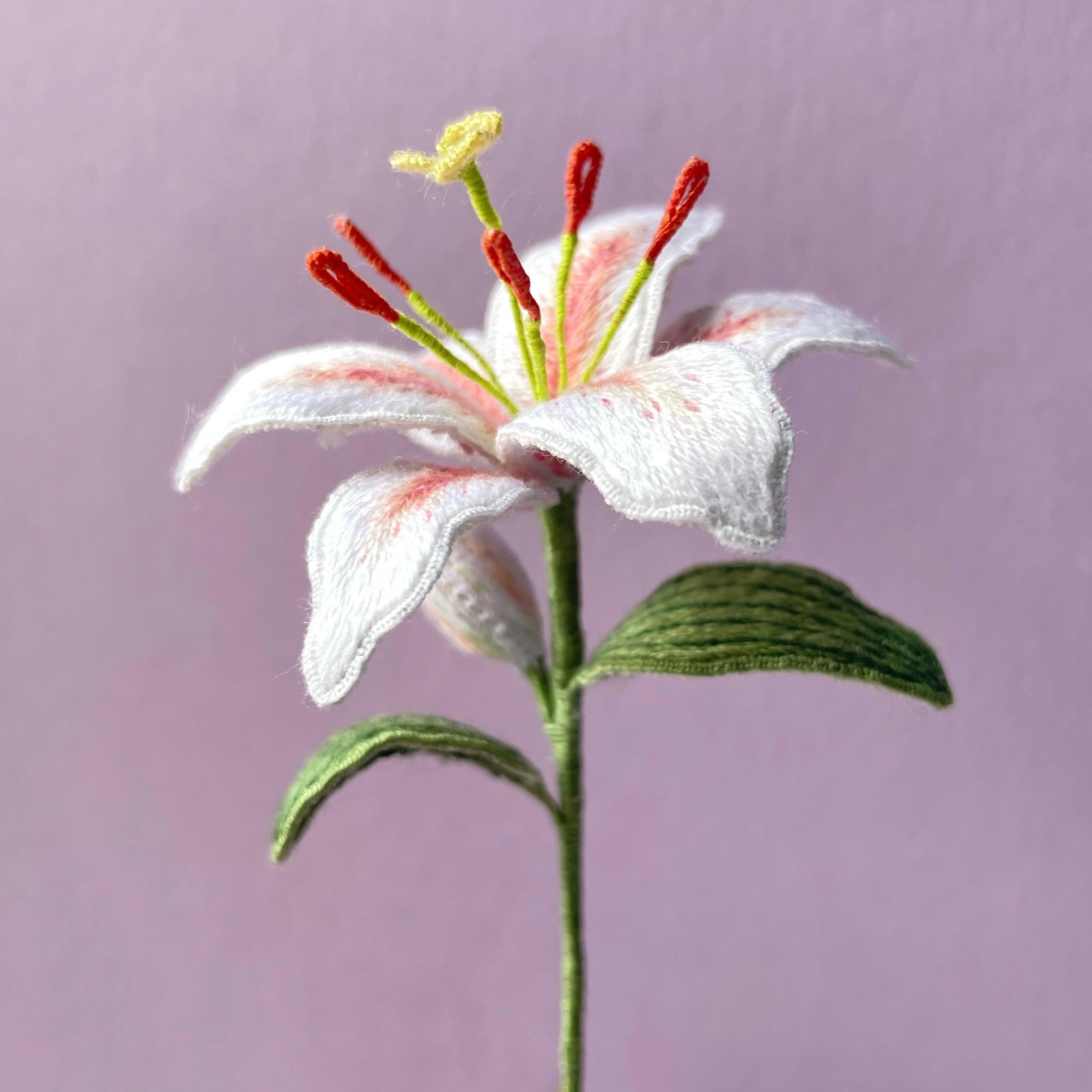 Embroidered white lily flower with green leaves on a purple background.