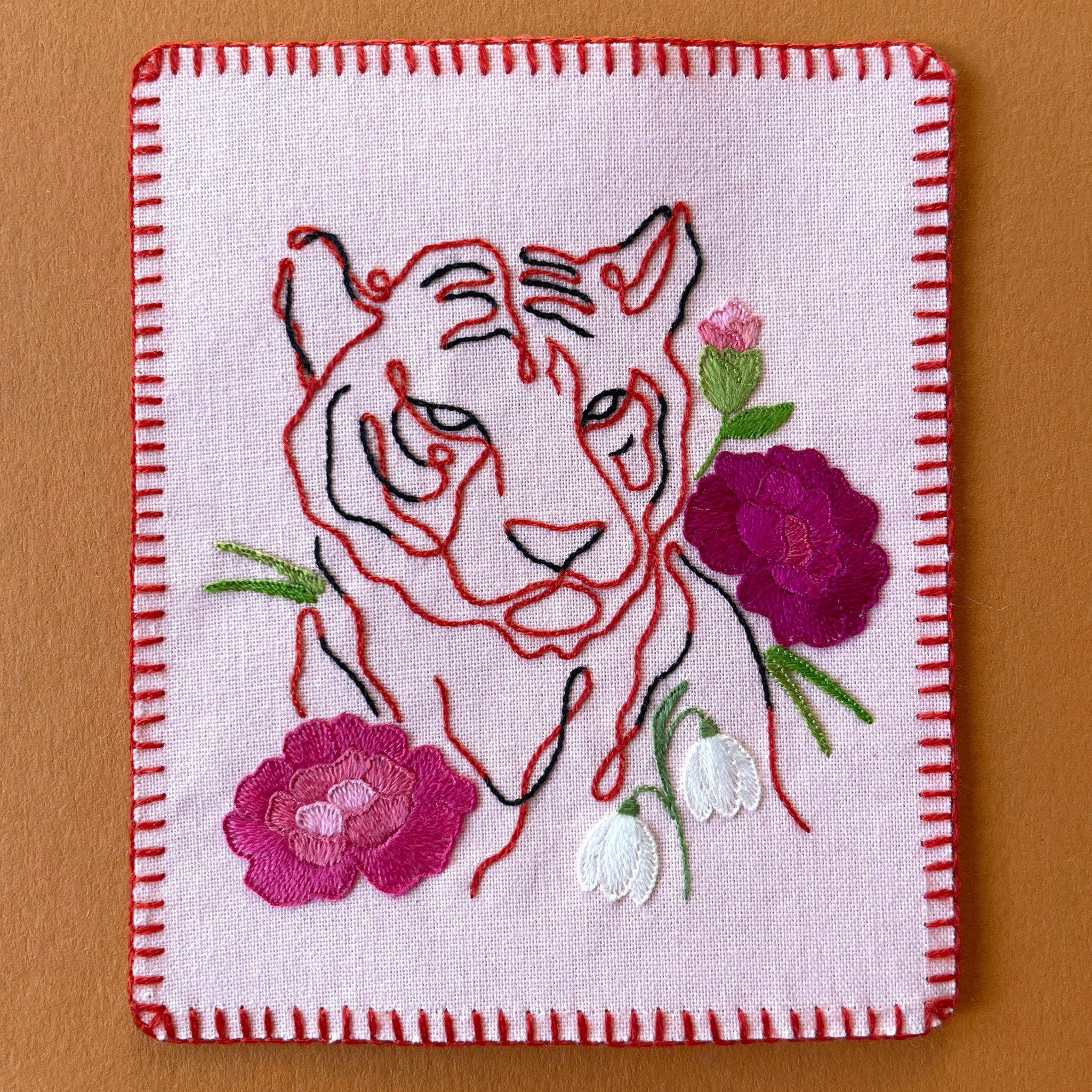 Embroidery of a tiger's face with pink and purple flowers on a white fabric background.