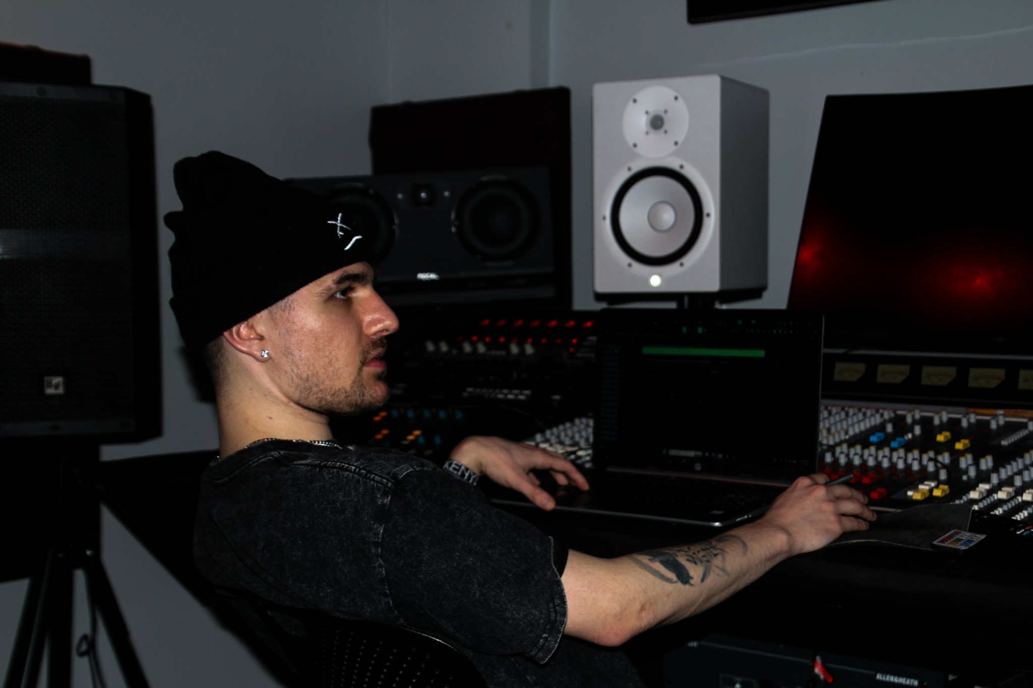 Person wearing a black beanie working with audio equipment in a studio.