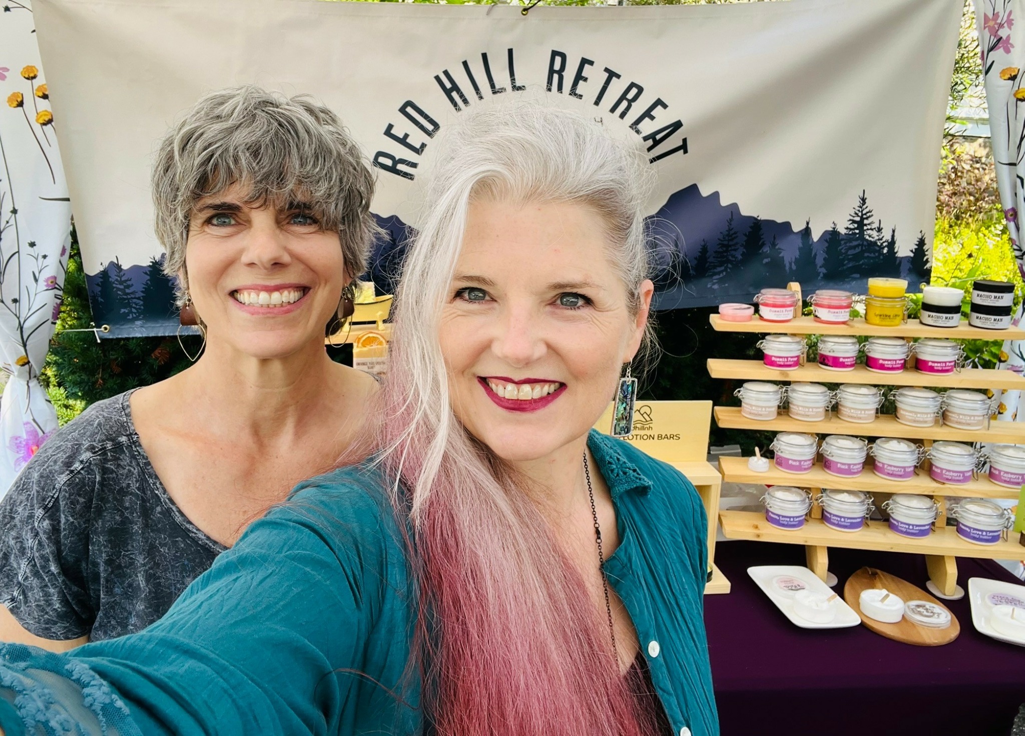 Two women smiling in front of a display with cupcakes and a banner reading 'Red Hill Retreat'.