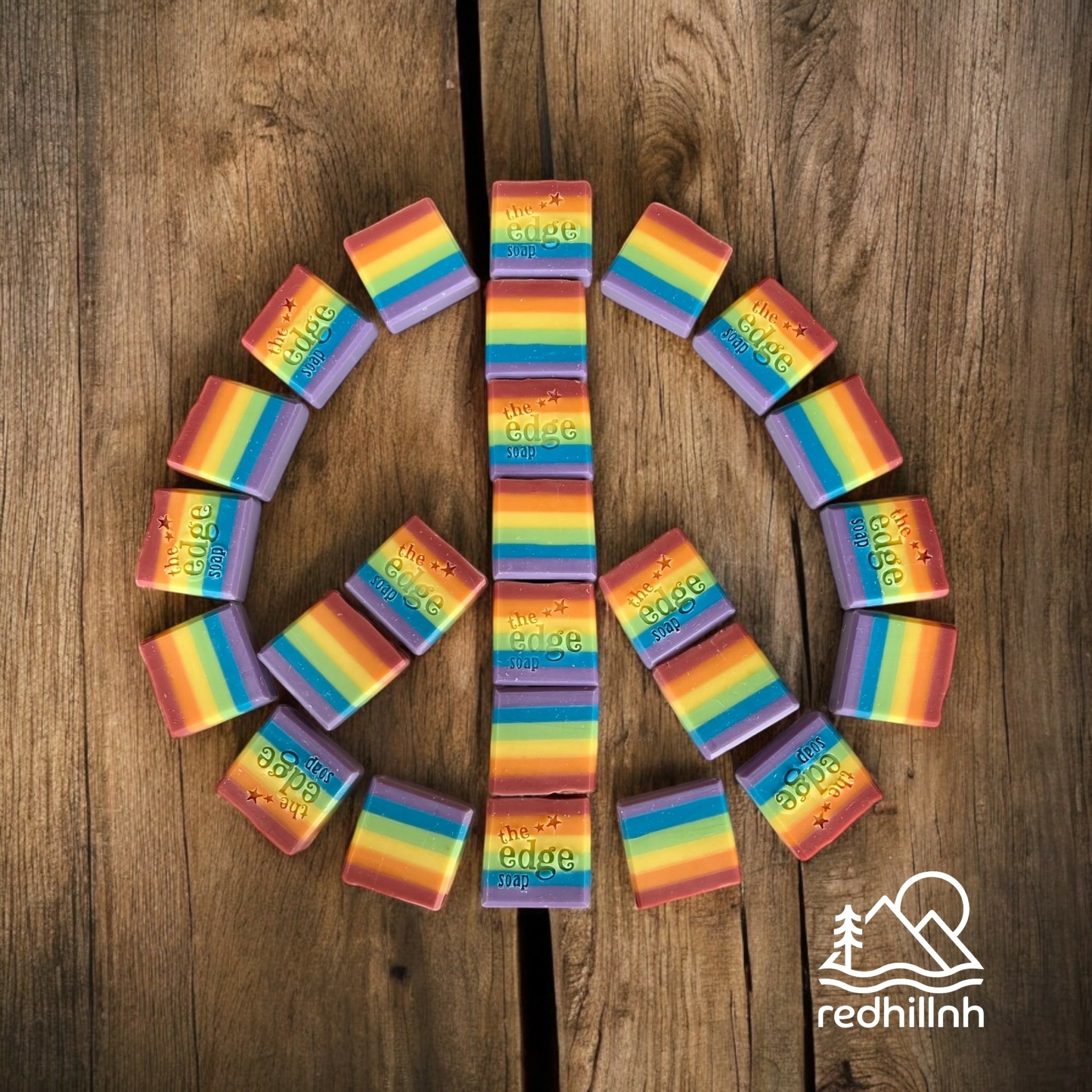 Rainbow-colored rectangular blocks arranged in a circle on a wooden surface, with a white logo in the bottom right corner.
