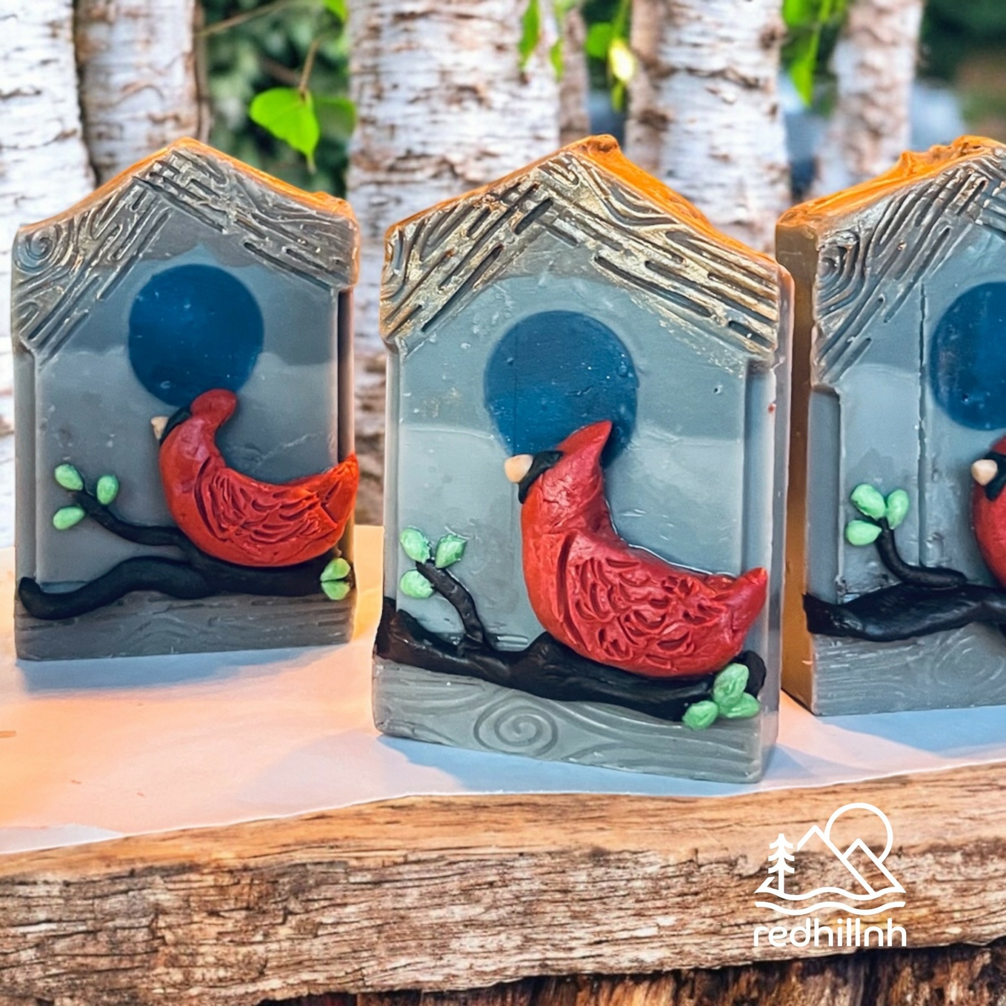 Three decorative glass blocks with red and black abstract designs, set on a wooden surface with trees in background.