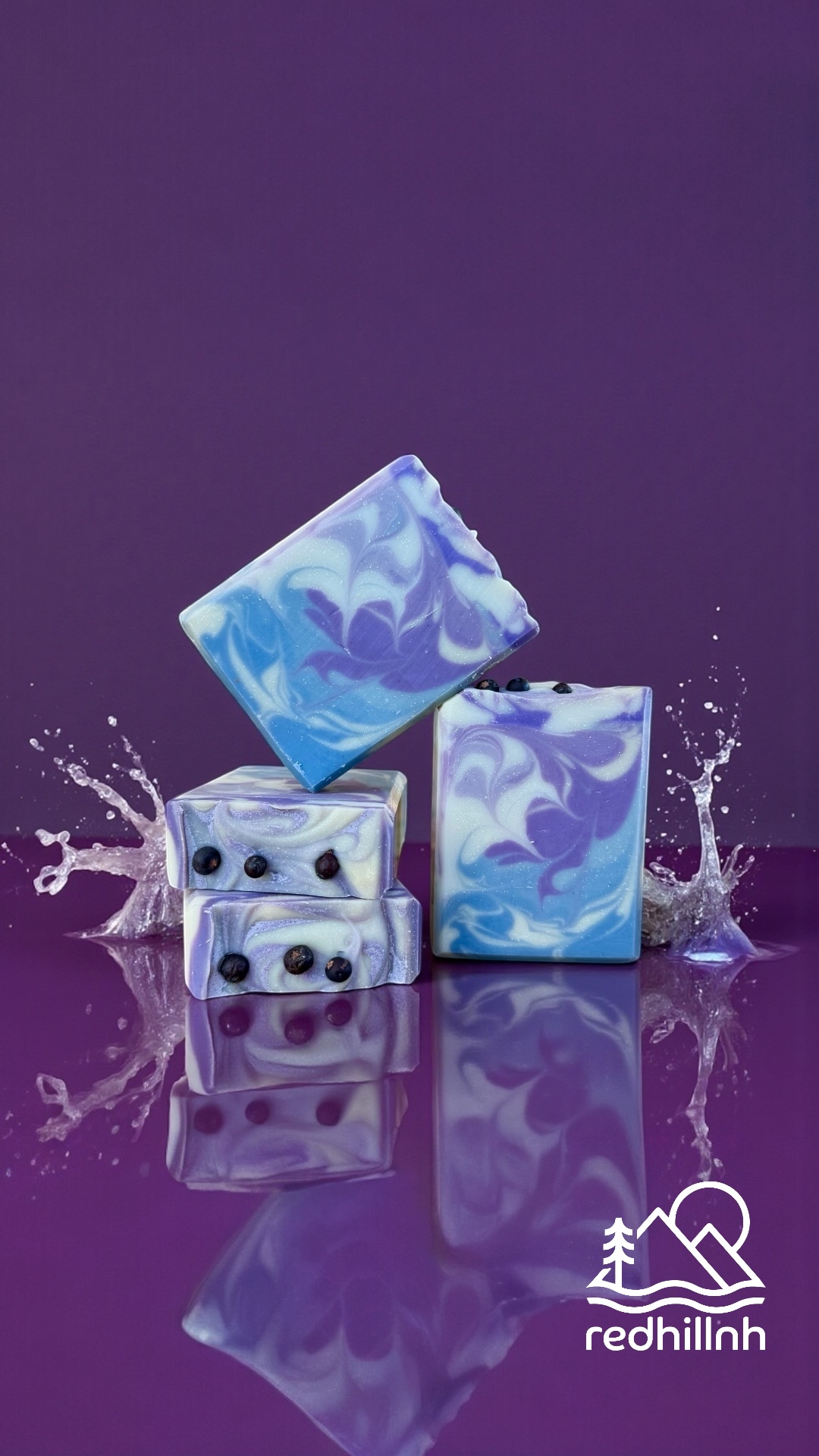 Four marbled soap bars with water splashes on a purple background.