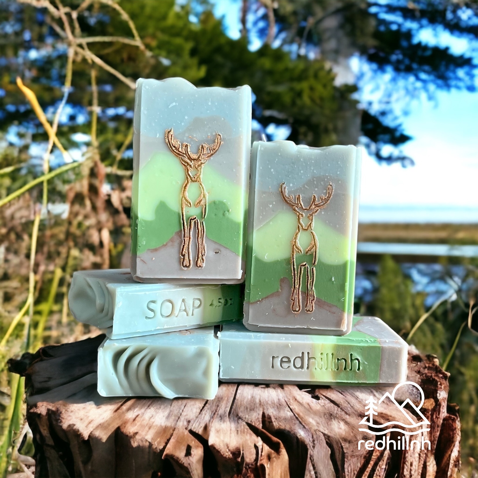 Two soap bars with deer designs, placed on a tree stump outdoors with trees and sky in background.