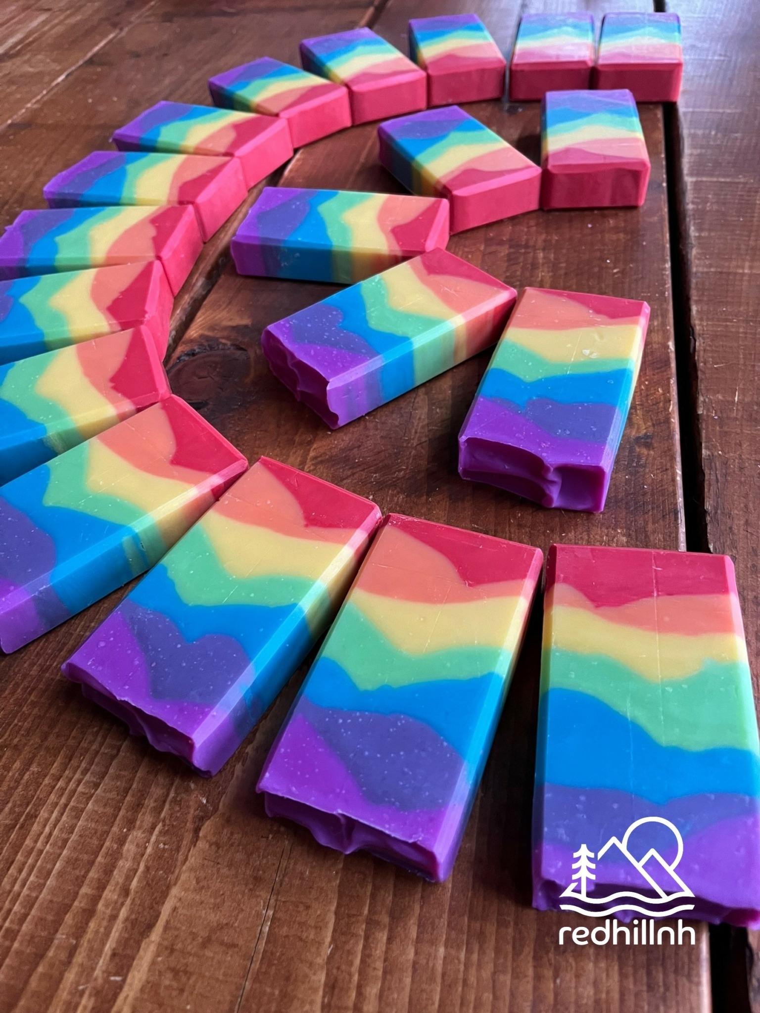 Colorful rainbow soap bars arranged in a semi-circle on a wooden surface.