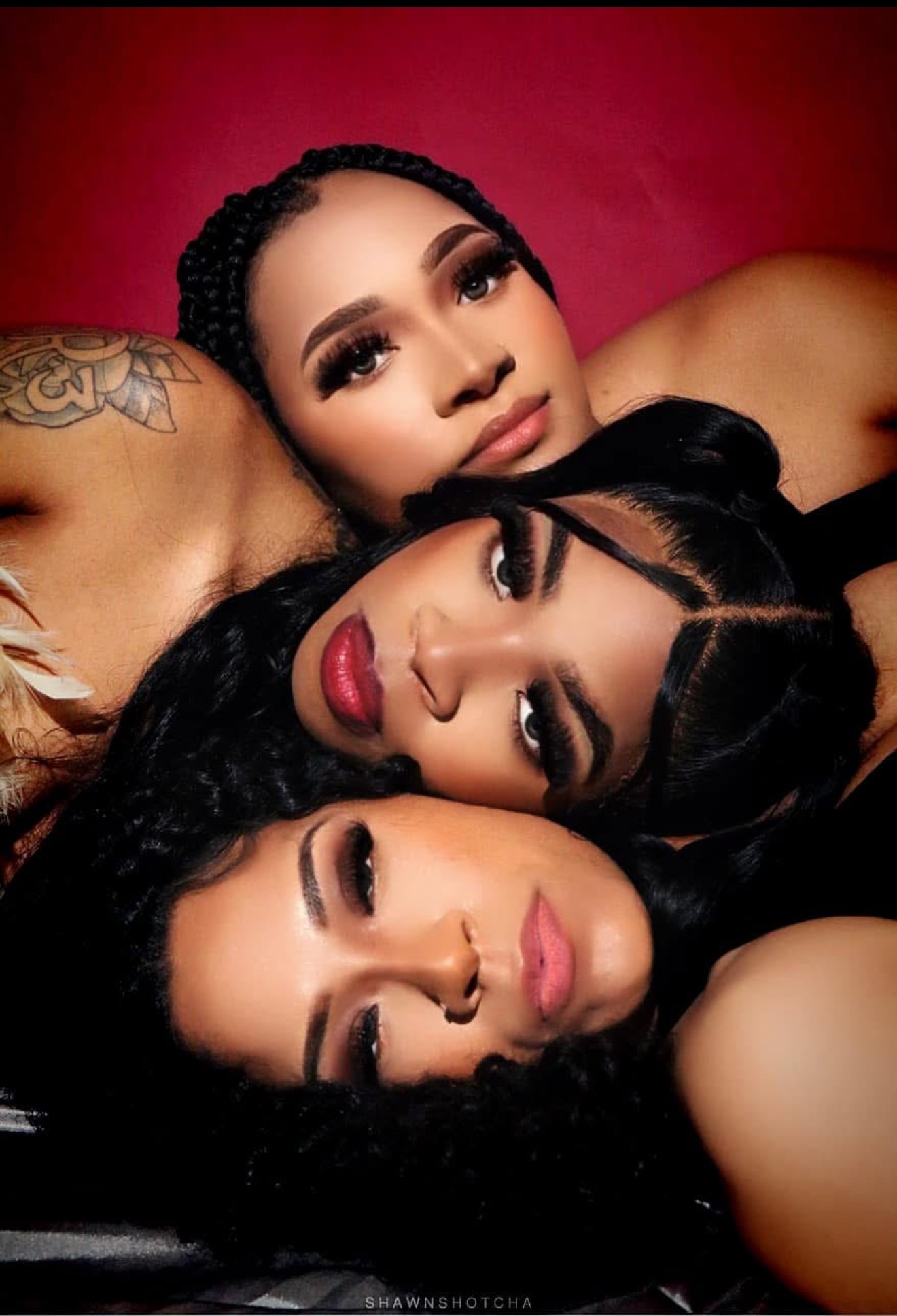 Three women with dark hair and makeup lying close together against a red background.
