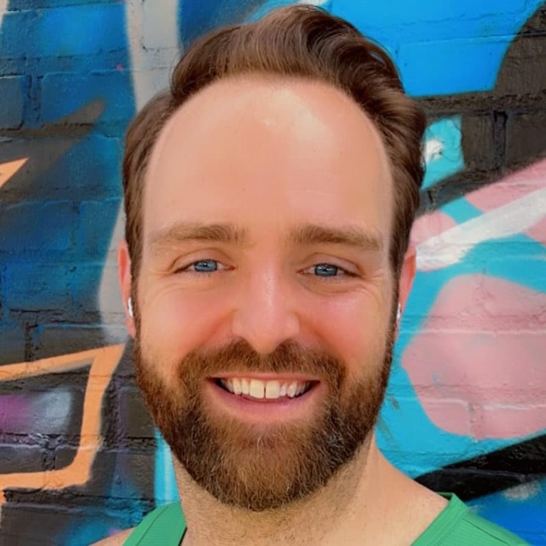 Man with brown hair and beard smiling in front of colorful graffiti background.