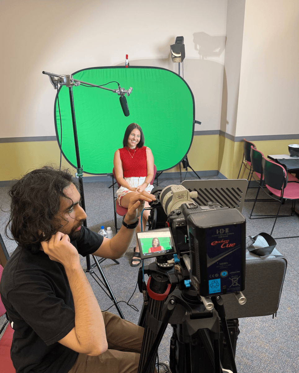 Person filming woman in front of green screen with camera equipment in room.