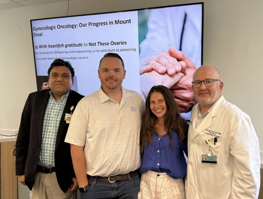 Four people standing in front of a presentation screen with text and an image of hands holding a stethoscope.