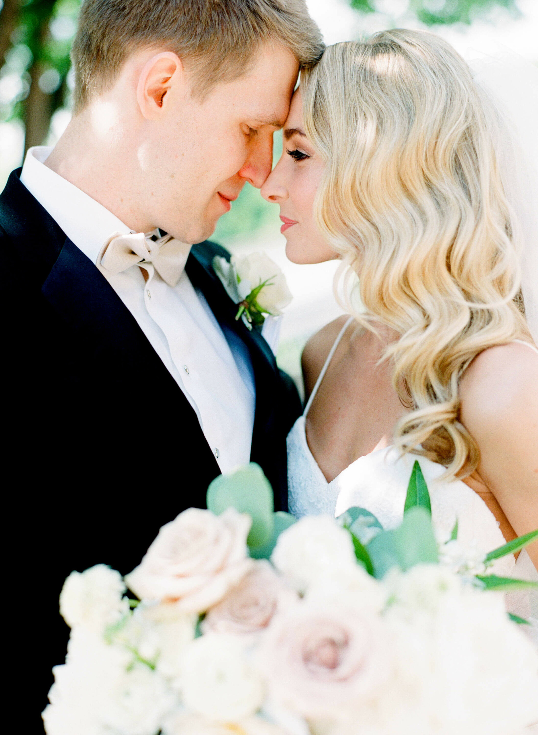 Close-up of a couple with foreheads touching, surrounded by flowers, in wedding attire.