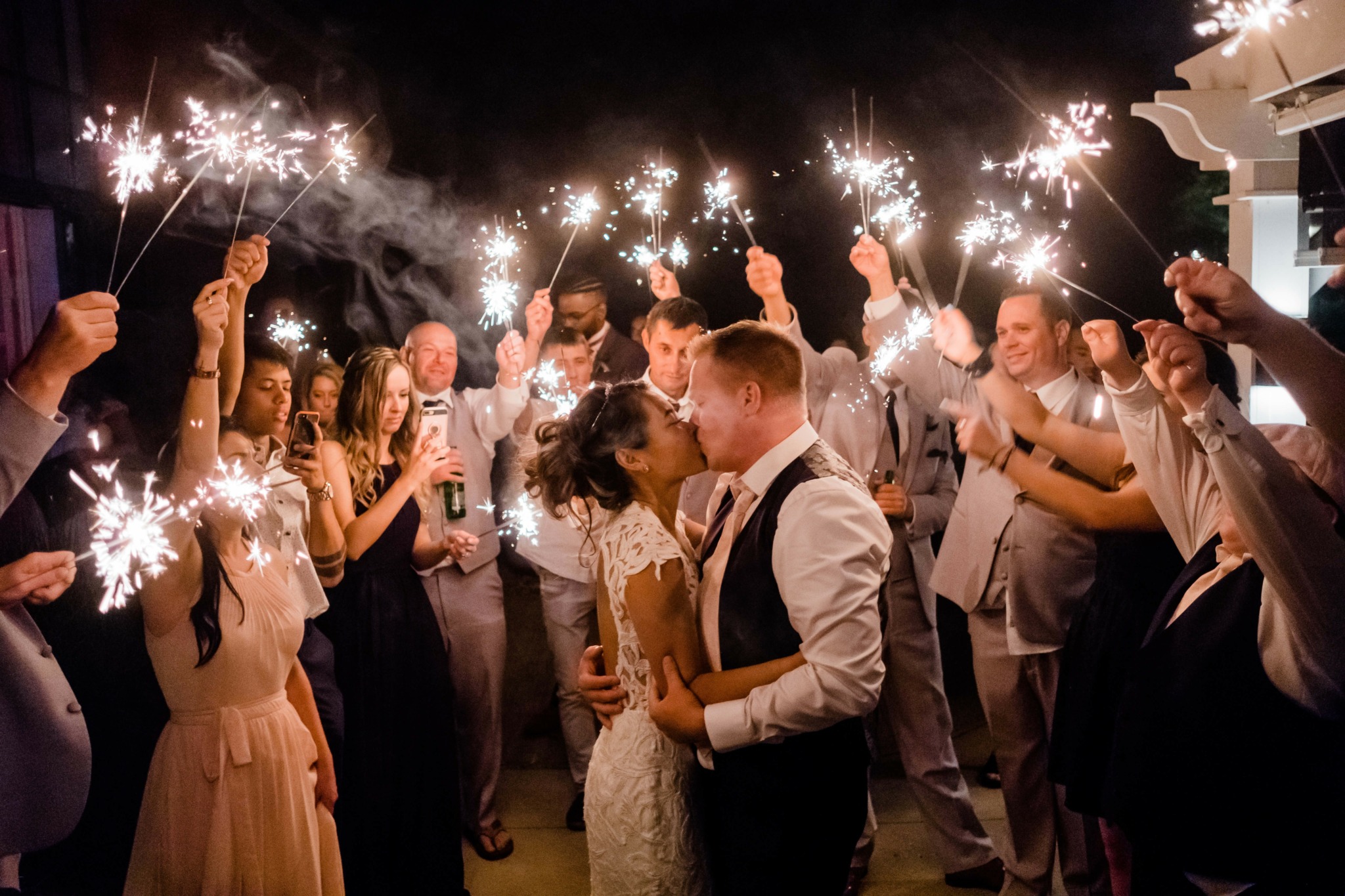 Couple dancing surrounded by people holding sparklers at night celebration, smiling and celebrating together.